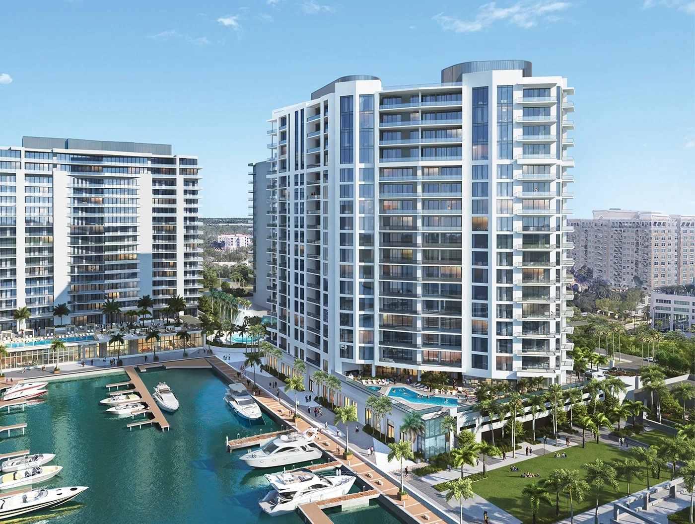 Sarasota Motor Club - Sports Car Rental Sarasota FL - A modern high-rise apartment complex next to a marina with boats, overlooking a park with people and trees, under a clear blue sky.