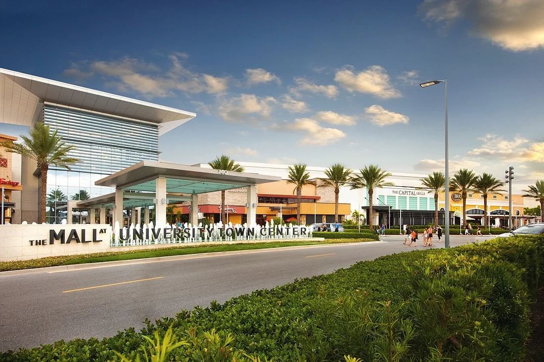 Sarasota Motor Club - Sarasota Luxury Car Rental - Exterior view of the Mall at University Town Center with palm trees, clear sky, and shoppers walking outside.