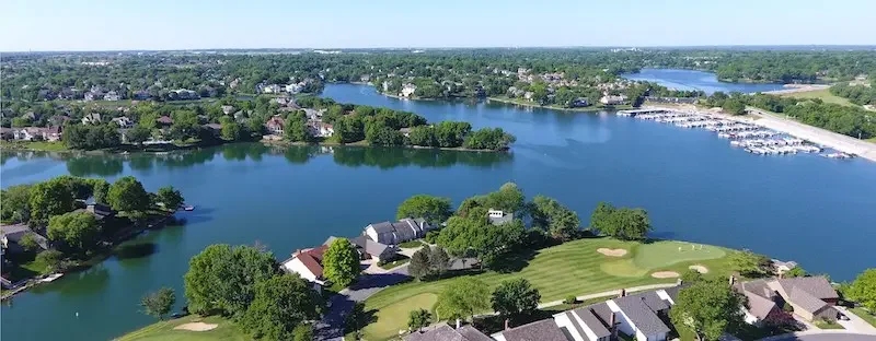 Sarasota Motor Club - Premium Car Service Sarasota - Aerial view of a suburban neighborhood with a large lake, houses, trees, and a golf course, under a clear blue sky.