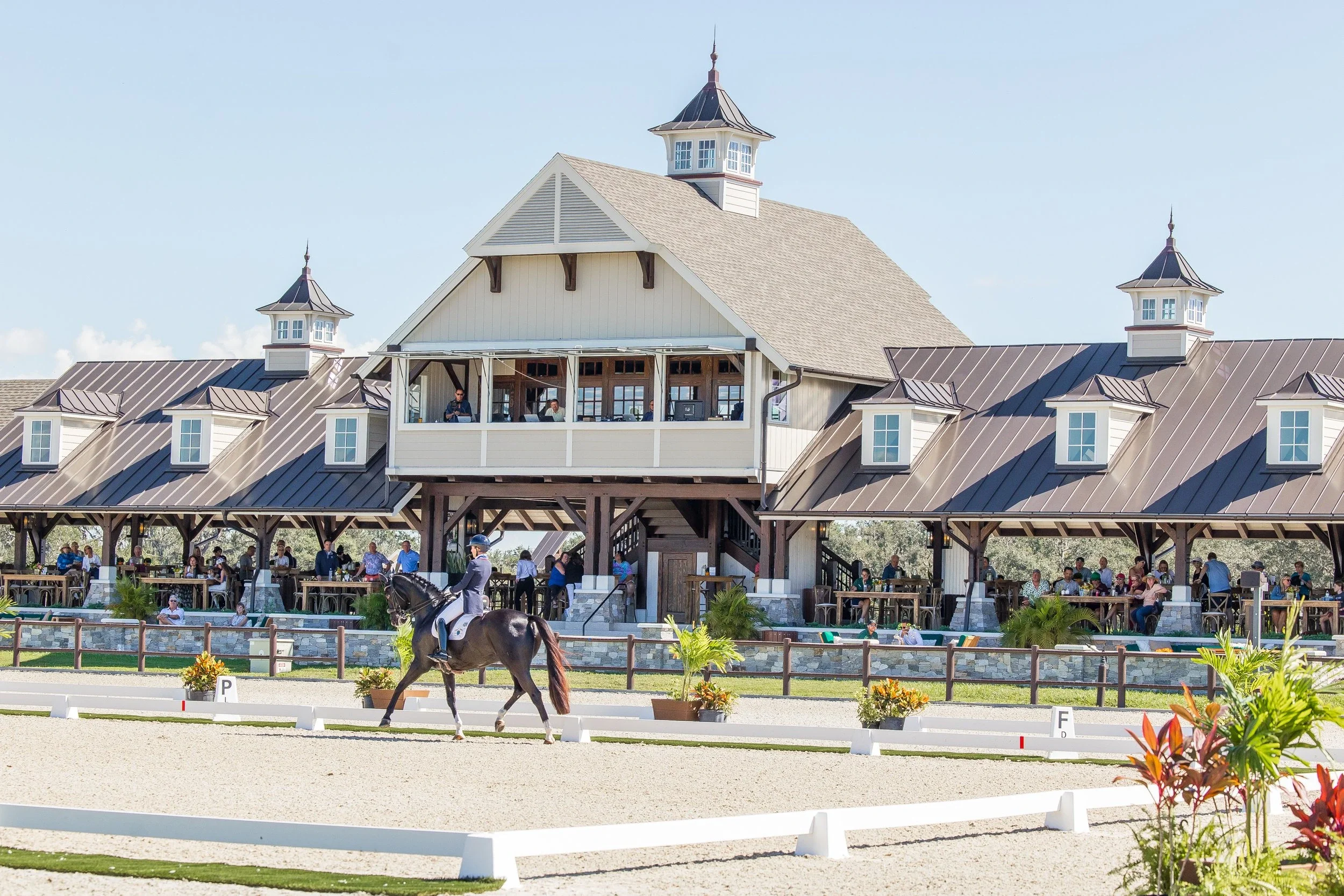 Sarasota Motor Club - Sports Car Rental Sarasota FL - A horse and rider performing dressage in an outdoor arena with a large pavilion and spectators, under a clear blue sky.