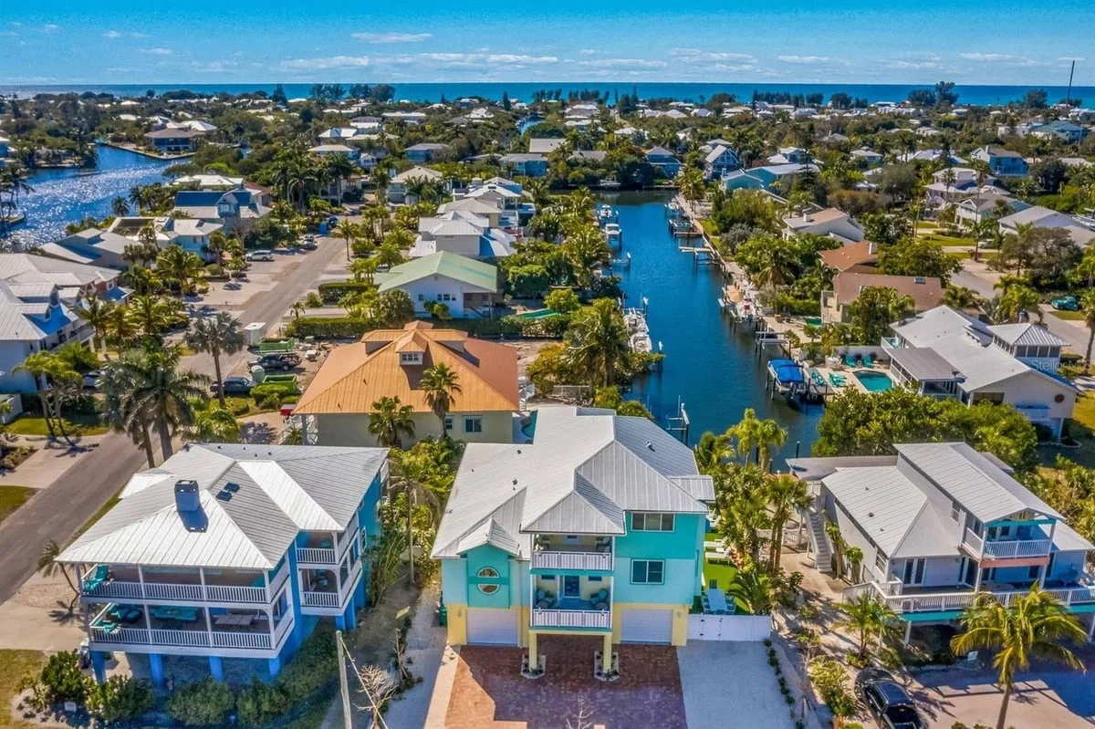 Sarasota Motor Club - Premium Car Service Sarasota - Aerial view of a coastal neighborhood with colorful houses, canals with boats, lush greenery, and the ocean in the background.