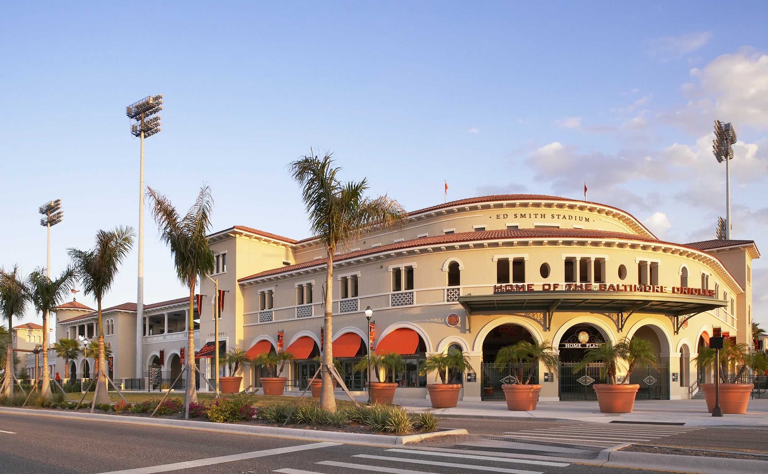 Sarasota Motor Club - Sports Car Rental Sarasota FL - Exterior view of Oriole Park at Camden Yards stadium in Baltimore, Maryland, with potted plants and palm trees in front, under a partly cloudy sky during sunset.