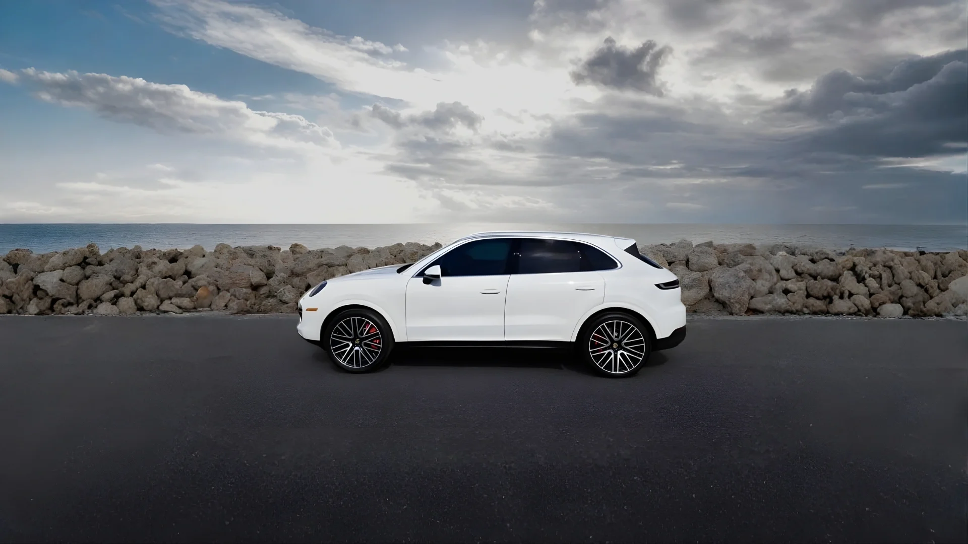 Sarasota Motor Club - Premium Car Service Sarasota - A white luxury SUV parked on a paved road near a rocky shoreline with the ocean and a cloudy sky in the background.