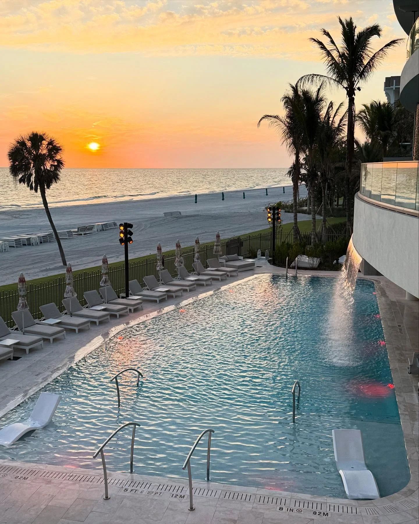 Sarasota Motor Club - Sarasota Luxury Car Rental -  A beachfront pool area at sunset, with chairs, umbrellas, palm trees, and the ocean in the background.
