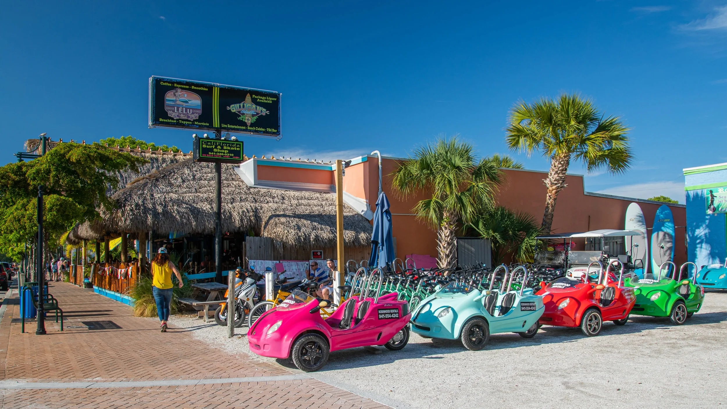 Sarasota Motor Club - Premium Car Service Sarasota - Colorful pedal cars parked outside a beachside tiki bar with palm trees.