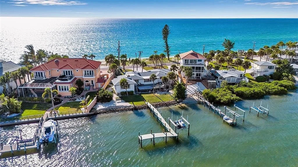 Sarasota Motor Club - Exotic Car Consignment Sarasota - Aerial view of waterfront houses with docks along a coastal area, with the ocean in the background and sunshine reflecting on the water.