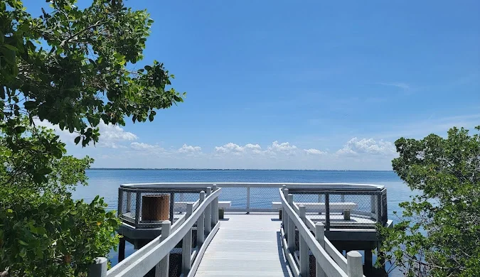 Sarasota Motor Club - Exotic Car Rental Sarasota Florida - A wooden dock extending over water, surrounded by green trees with a blue sky and clouds in the background.