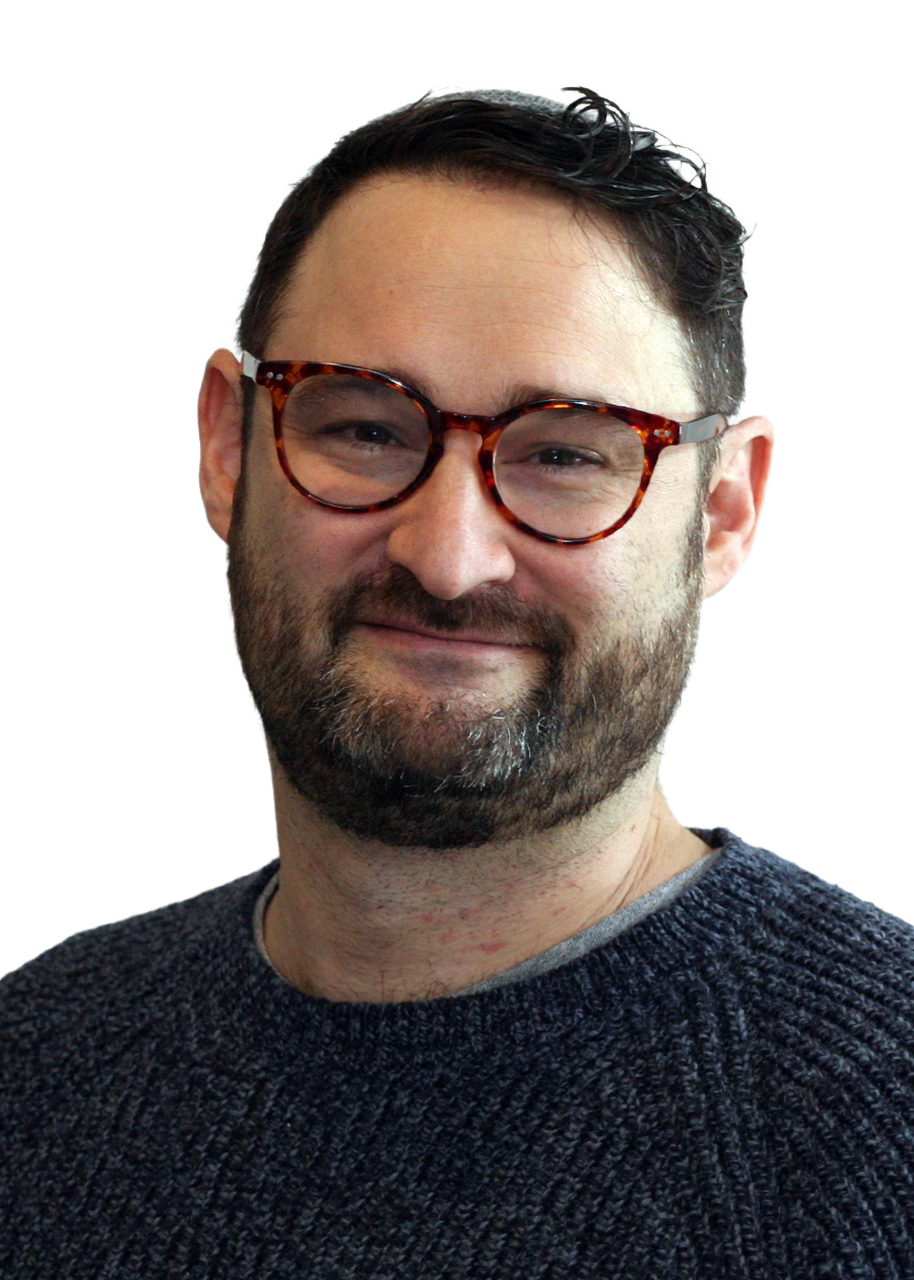 Close-up of a smiling man with glasses and a beard, wearing a dark knitted sweater.