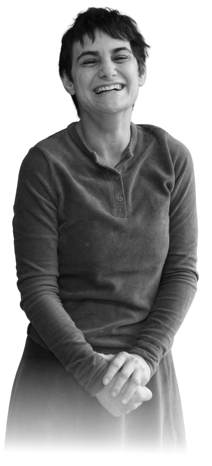 A woman with short dark hair smiling and holding her hands together in front of her, wearing a long-sleeve, button-up shirt.