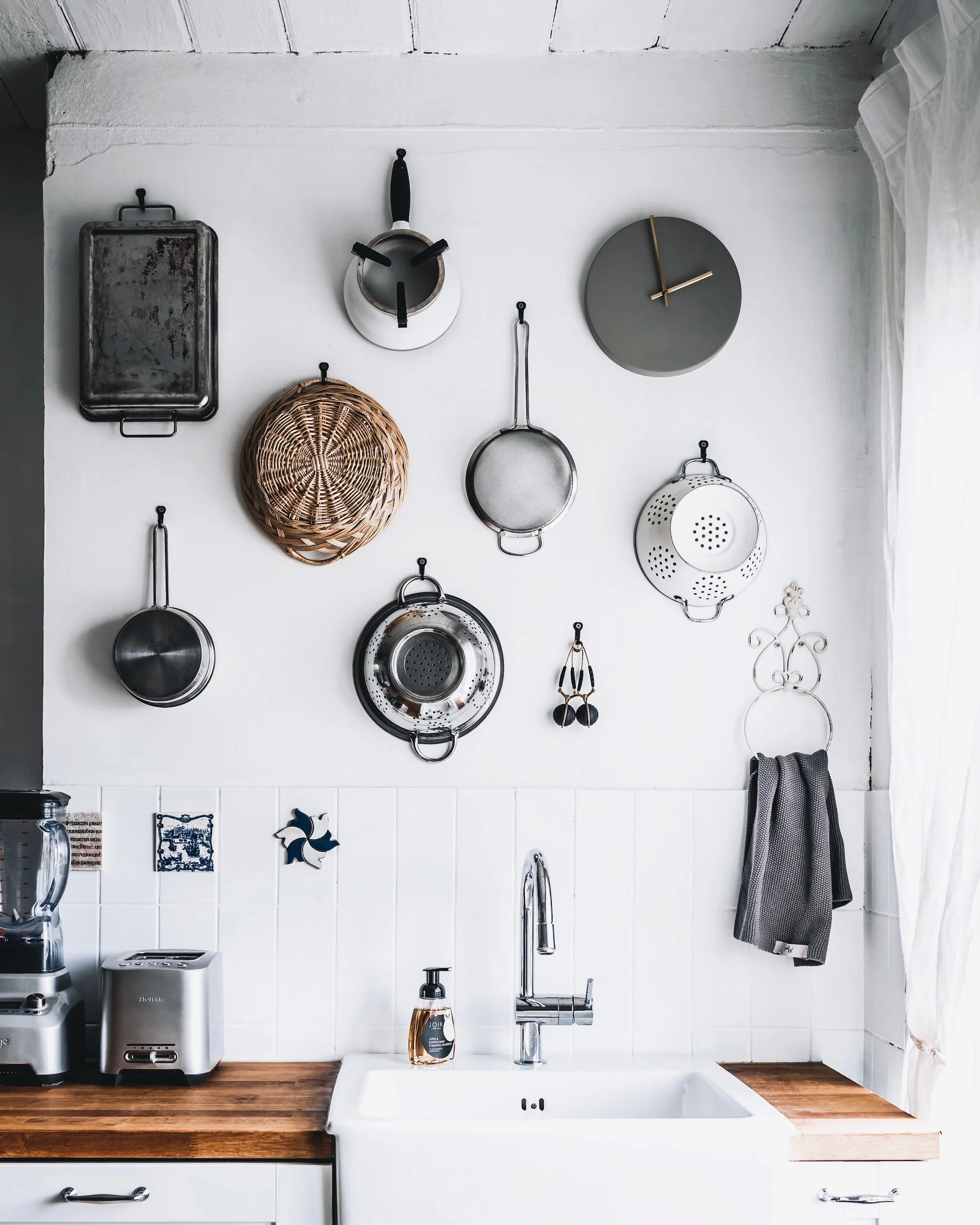 Valge köögisein, millele on dekoratsioonideks riputatud köögitarbed - korvid, sõelad, potid