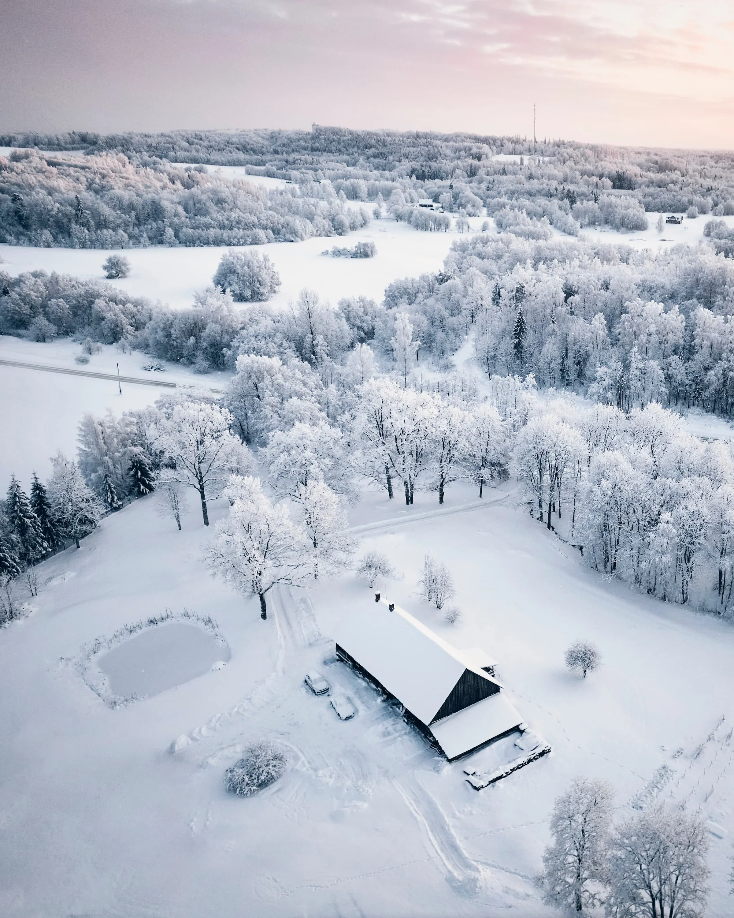 Õhuvaade lumisele Lõuna-Eesti maastikule taluhooviga loojanguvalguses