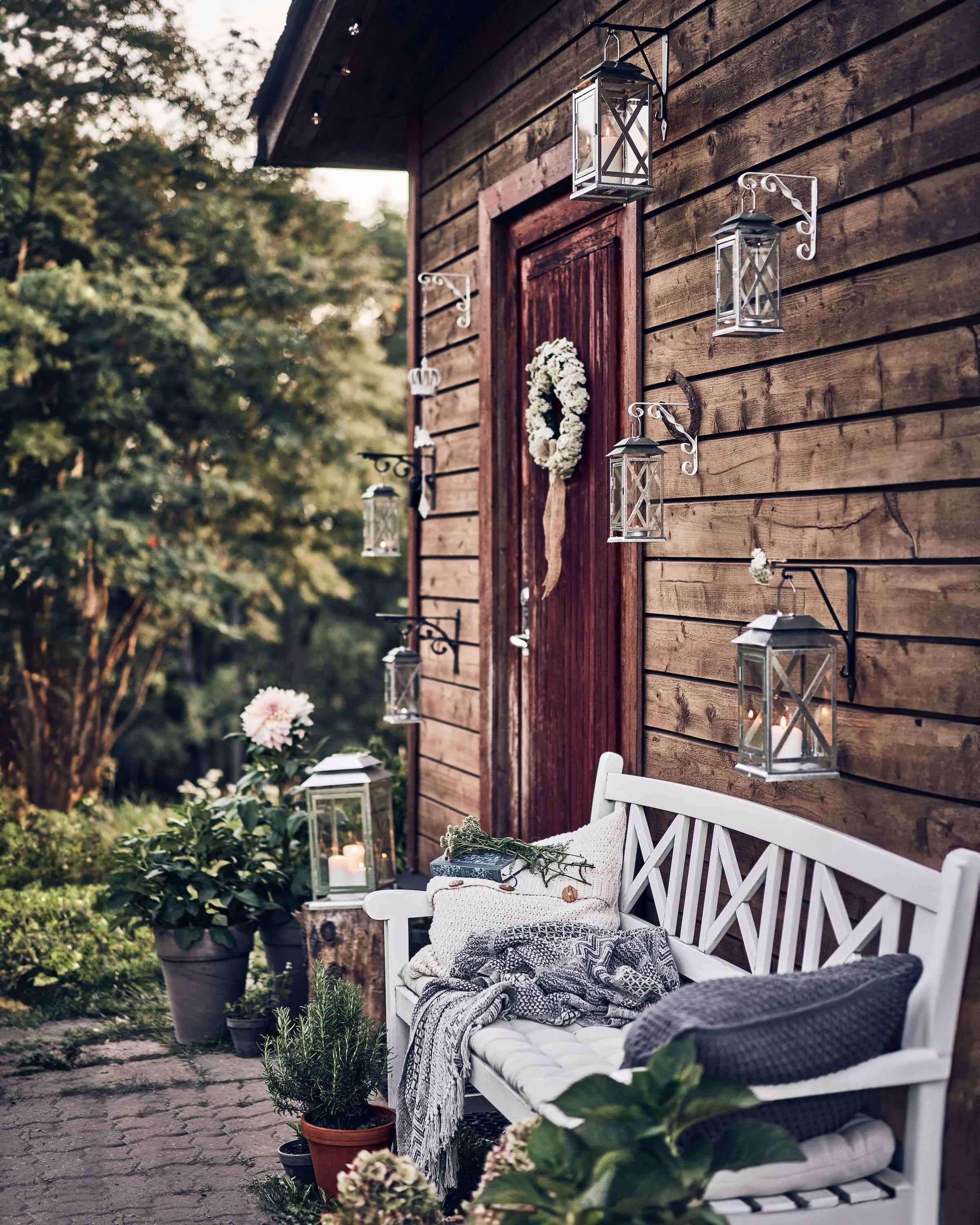 Suvine vaade pärjaga taluuksele, mida ümbritsevad laternad, õied ning patjadega valge pink