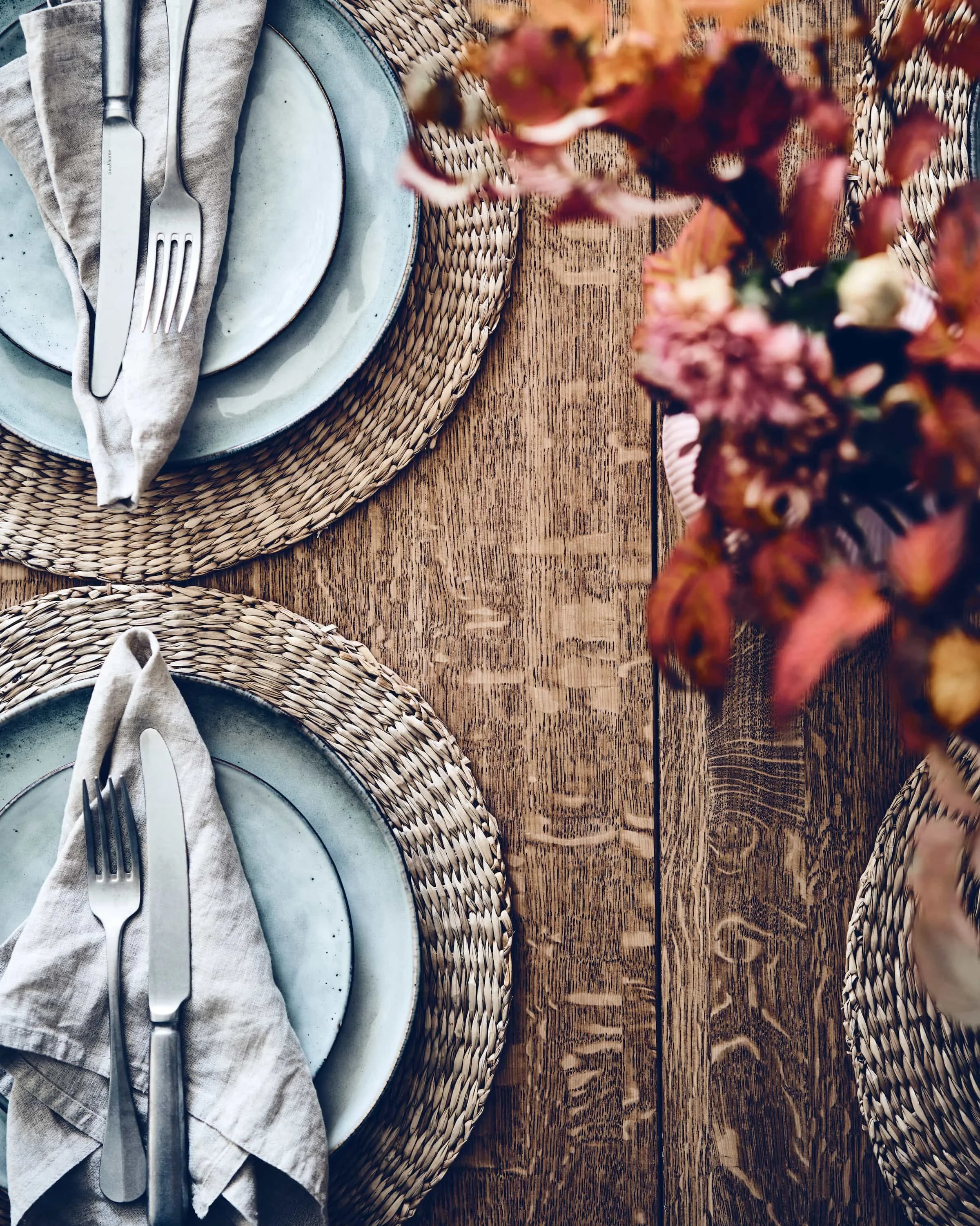 Kaetud söögilaud ülaltvaates hallikassinise keraamikaga, linaste rätikute ja sügisese lilleseadega