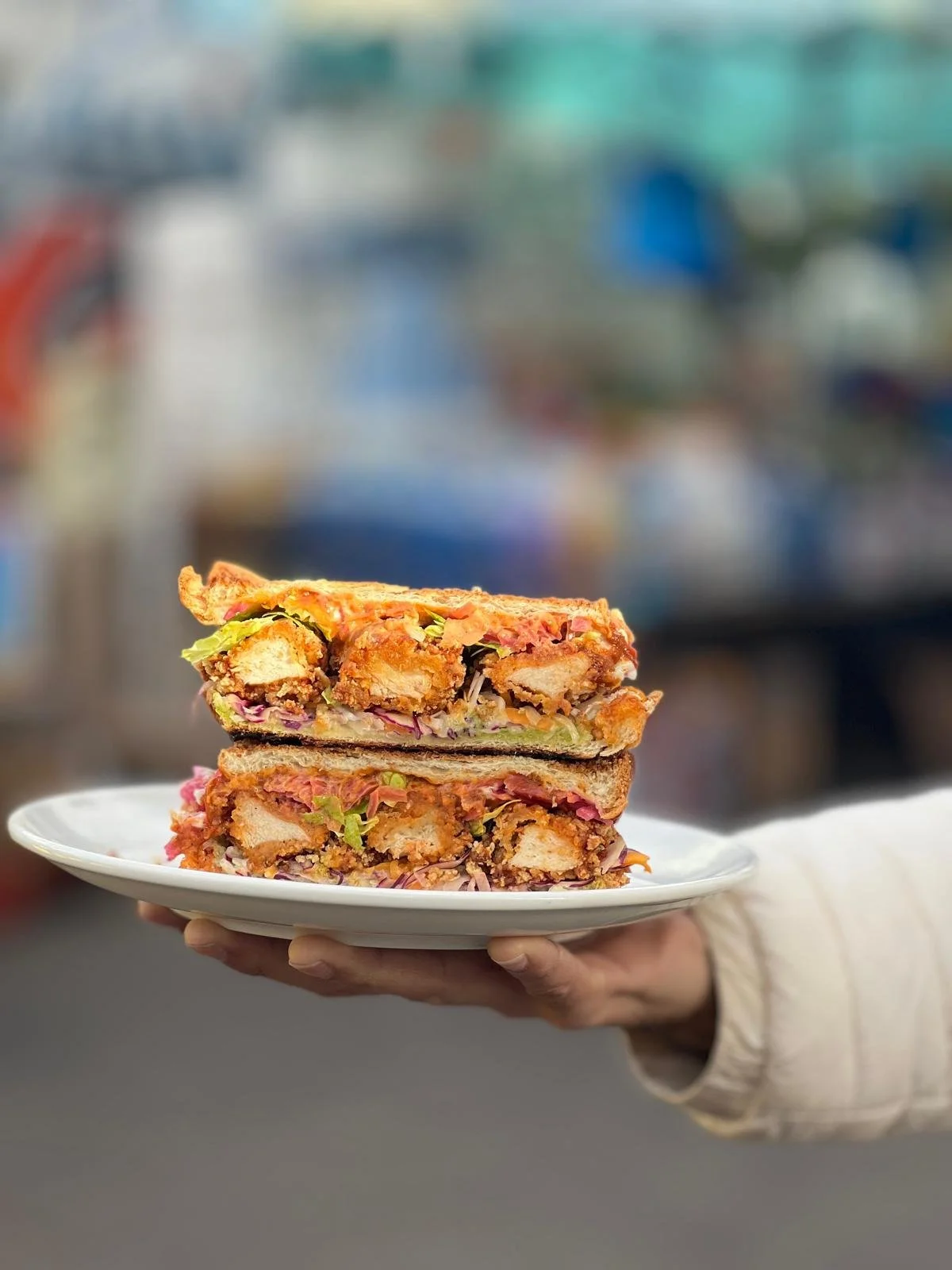 Deux sandwichs empilés sur une assiette, avec de la viande, de la salade, du pain, et des condiments, tenus par une main.