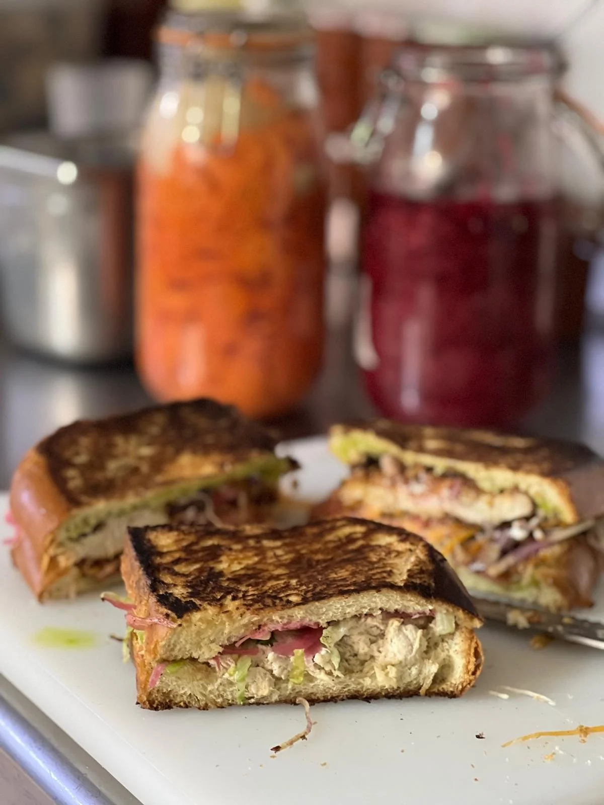 Sandwich grillé avec du jambon et de la laitue sur une assiette, en arrière-plan deux bocaux de confiture ou de compote.