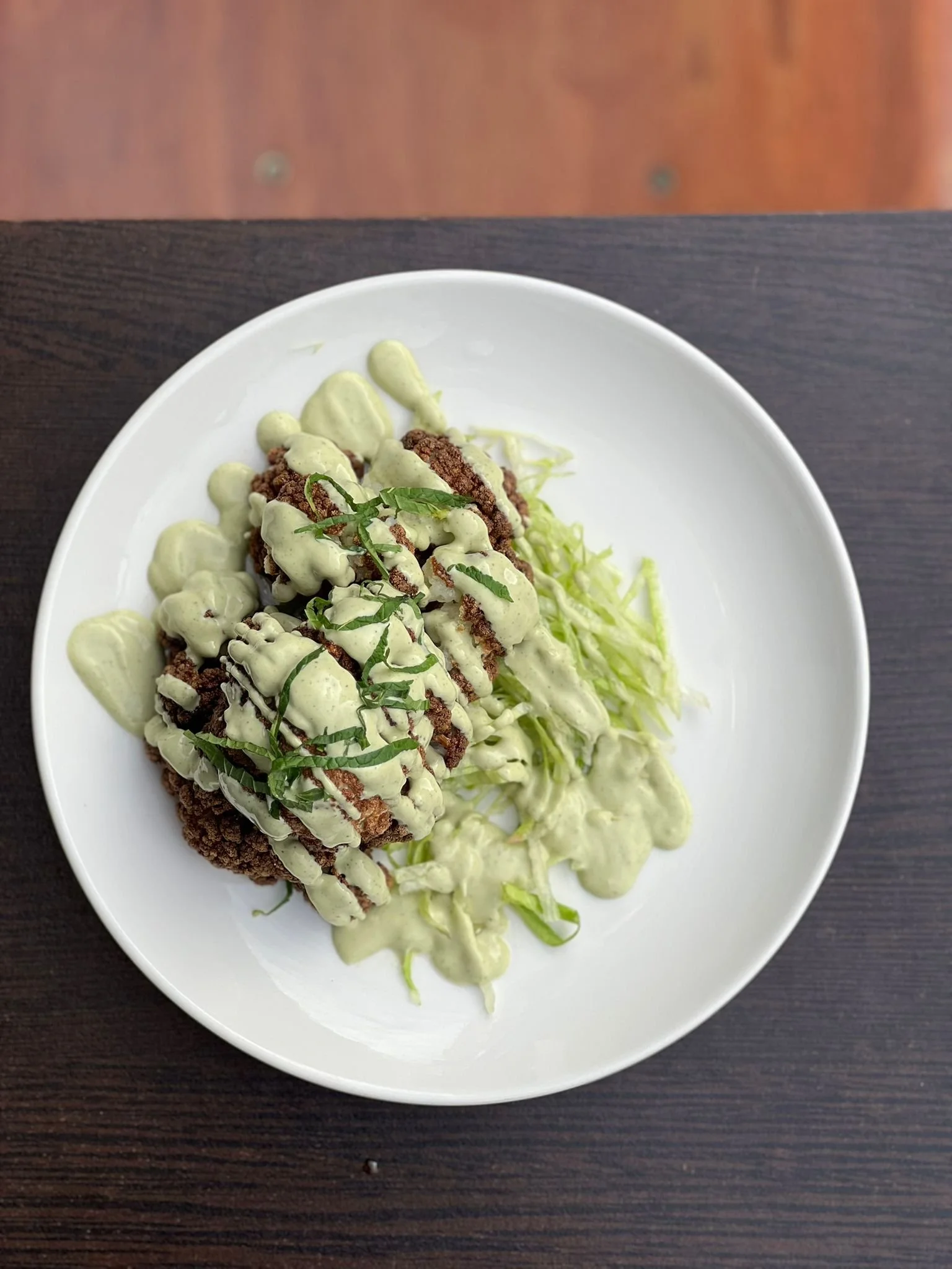 Plat de viande avec sauce verte, servi avec des légumes, le tout présenté dans une assiette blanche.