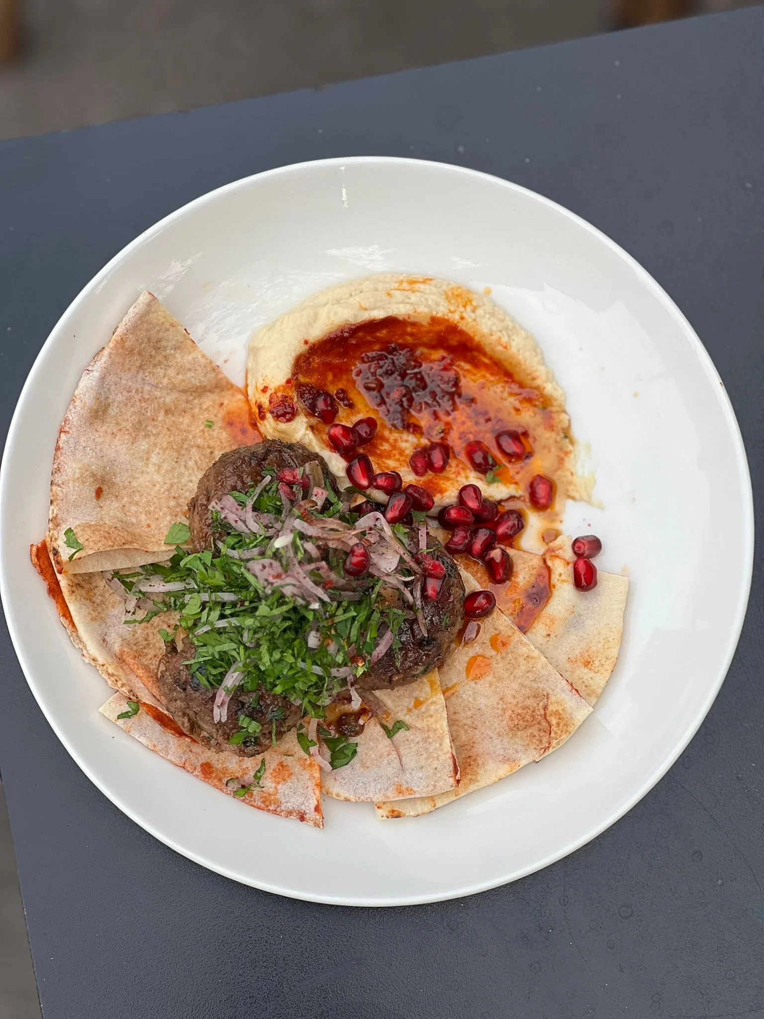 Plate avec un plat de kibbeh, houmous, pains pita, granatap жем, et garnitures.