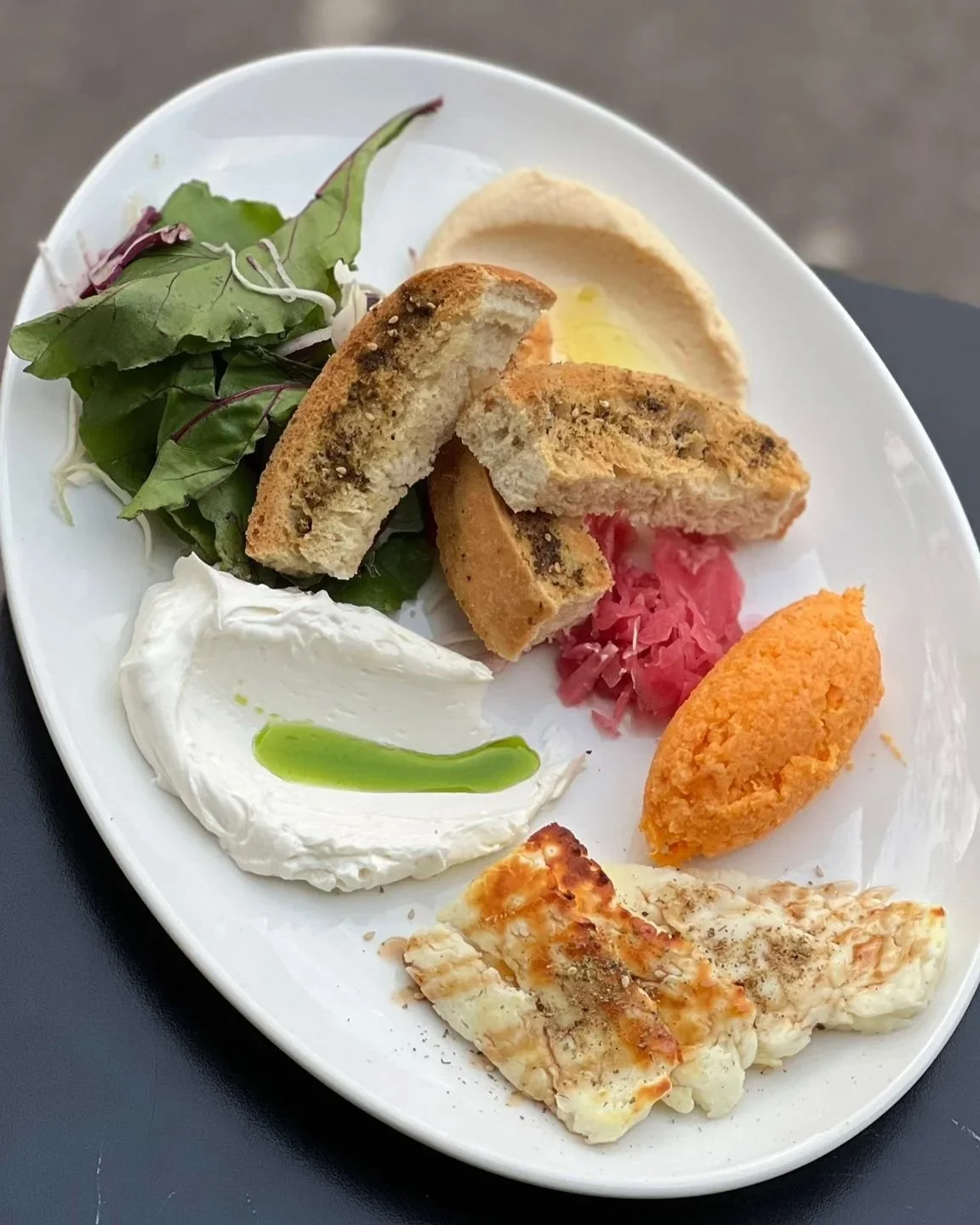 Assiette de mezze avec salade verte, houmous, pain pita, tzatziki, falafel, fromage, saumon grillé, et garlicky dip.
