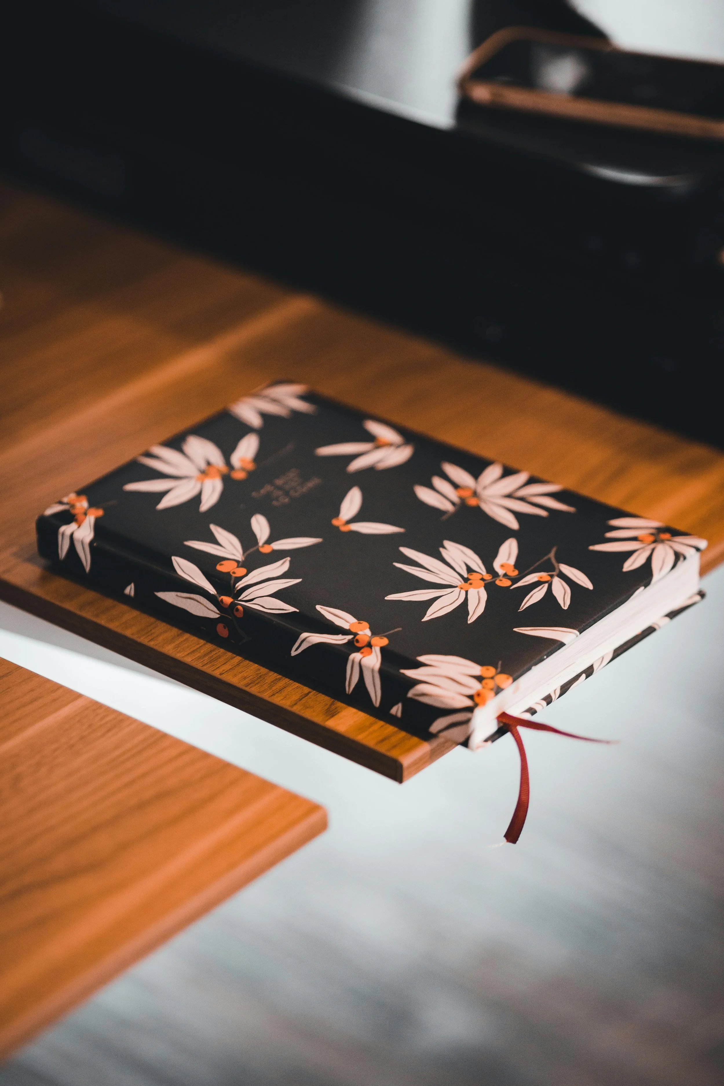 Un carnet à couverture noire avec un motif floral rose et orange posé sur une surface en bois.