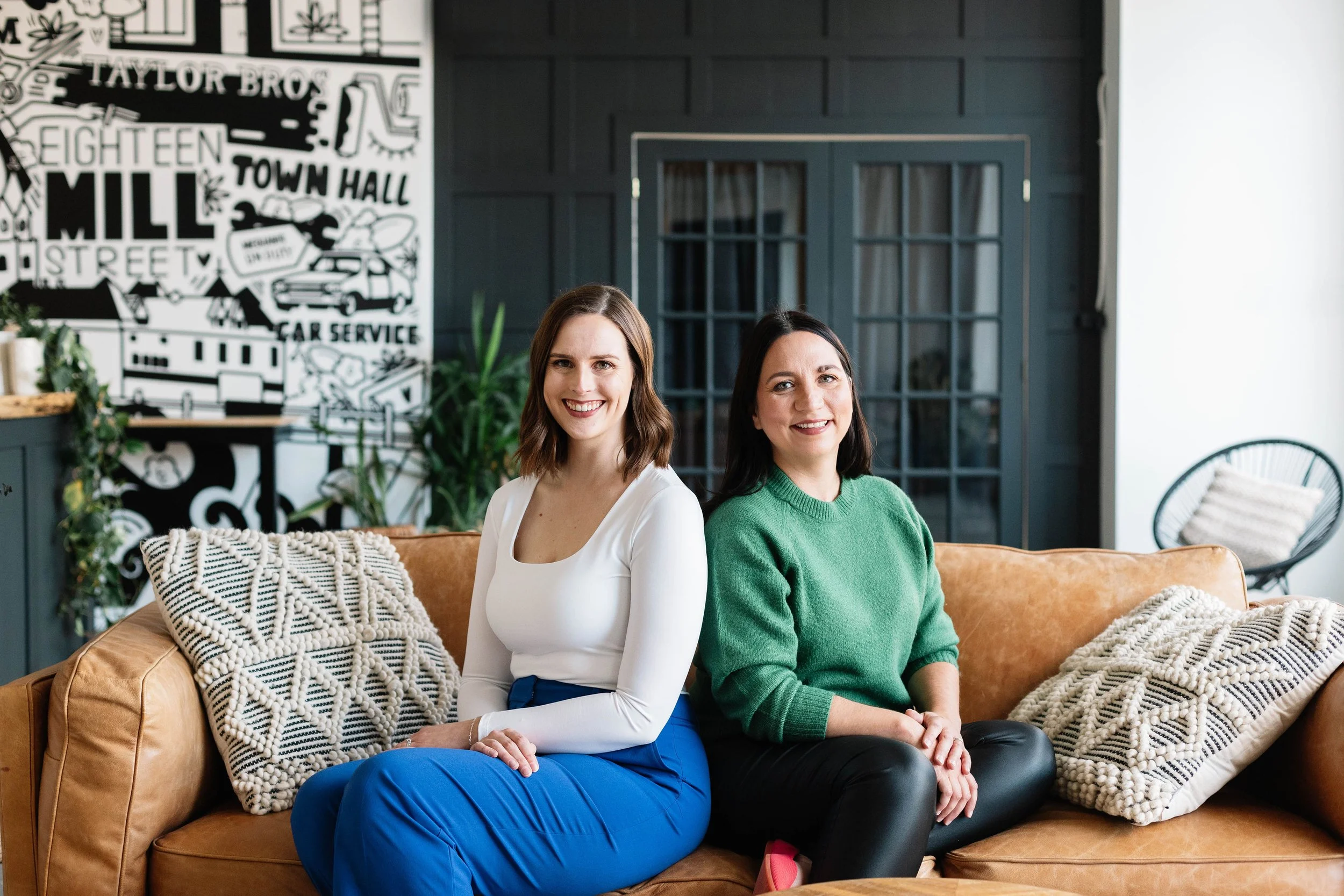 Megan Patterson and Natalie Cox, co-owners of CPI Interiors, an Ottawa interior design firm are sitting on a sofa.
