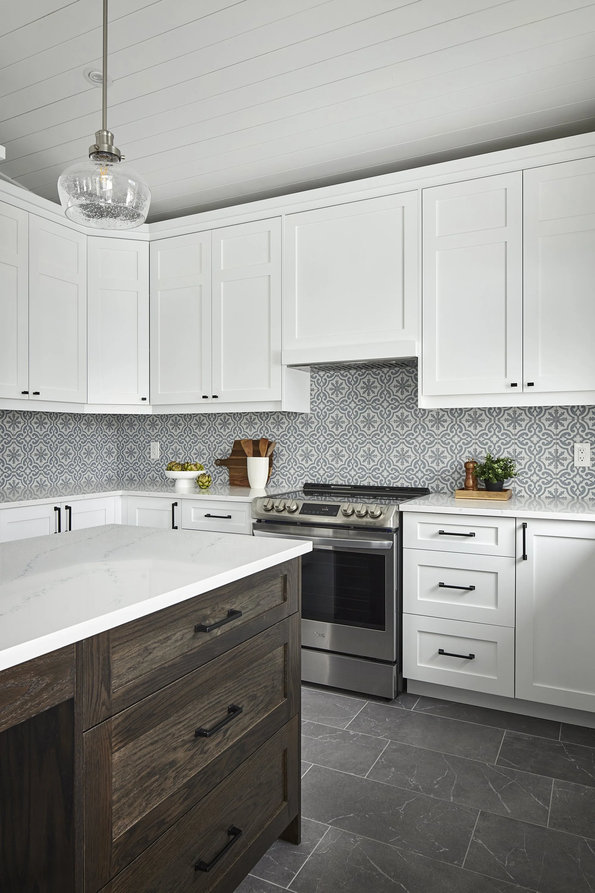 Custom kitchen renovation in Ottawa featuring white shaker cabinets, a patterned black splash in shades of white and blue and a charcoal grey tiled floor. 