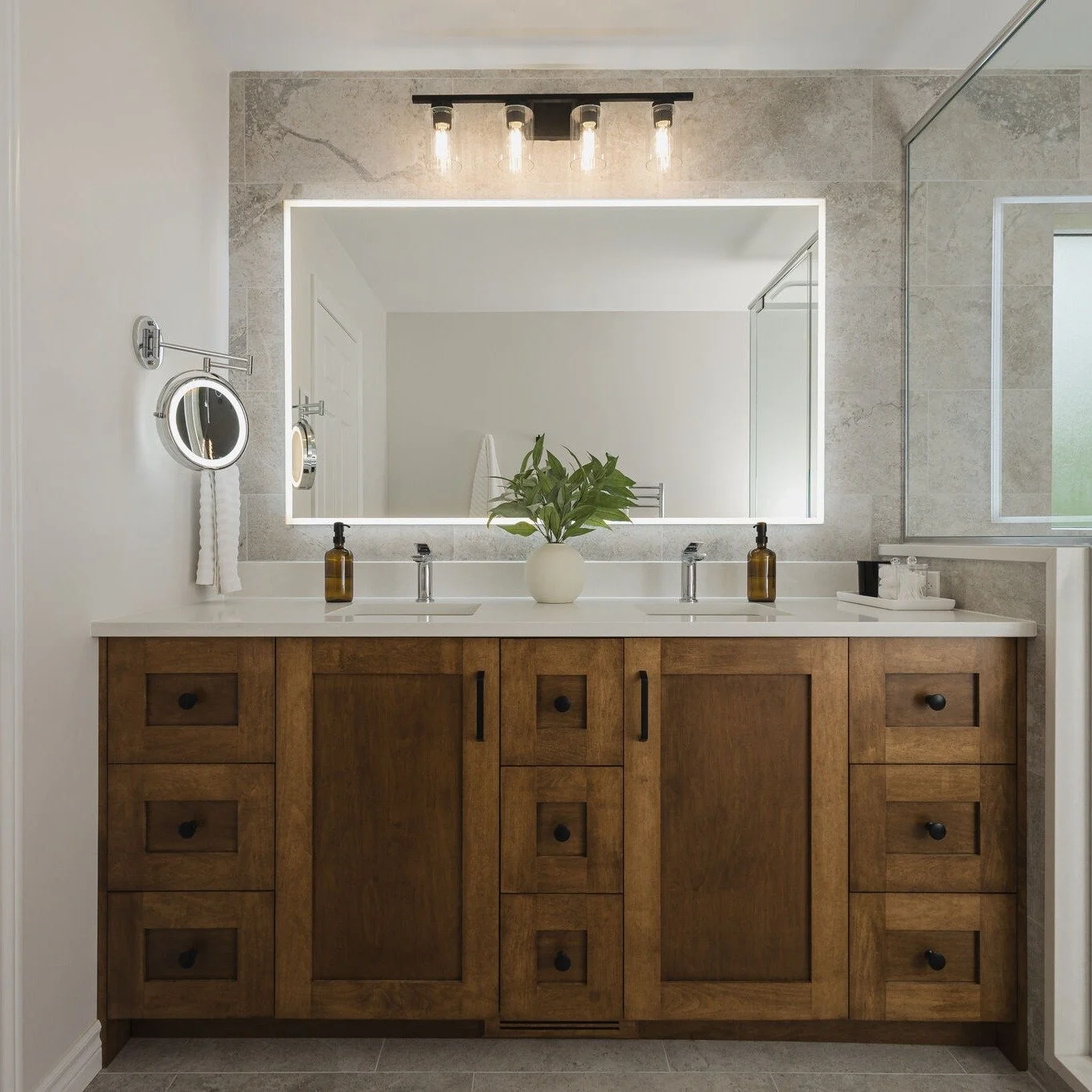We transformed this dated bathroom into a spa-like retreat, adding a double vanity, double shower, and thoughtful features like heated floors and hair tool storage. Every choice - from the charcoal chevron accent to the stone-look tile - was made to 