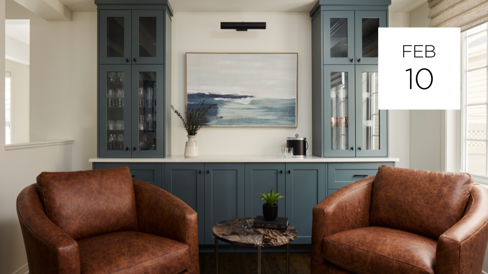 Living room with two brown leather armchairs facing a small round table with a potted plant, blue cabinets with glass doors, a vase with greenery, a picture on the wall, and large windows with blinds. Date overlay: February 10.