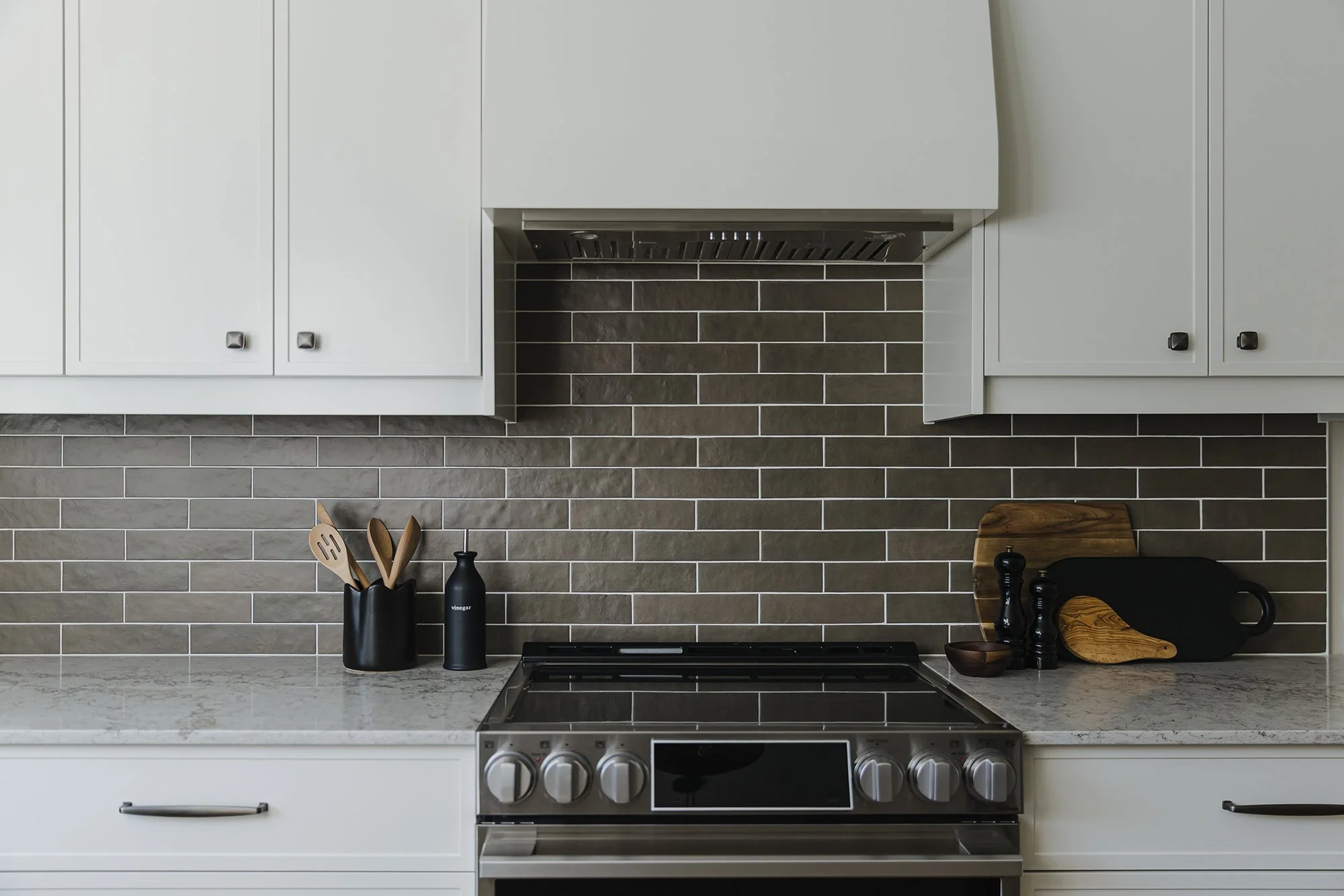 Custom kitchen design for an Ottawa family home featuring light coloured skinny shaker cabinets, a custom hood fan and a dark brown subway backsplash. 