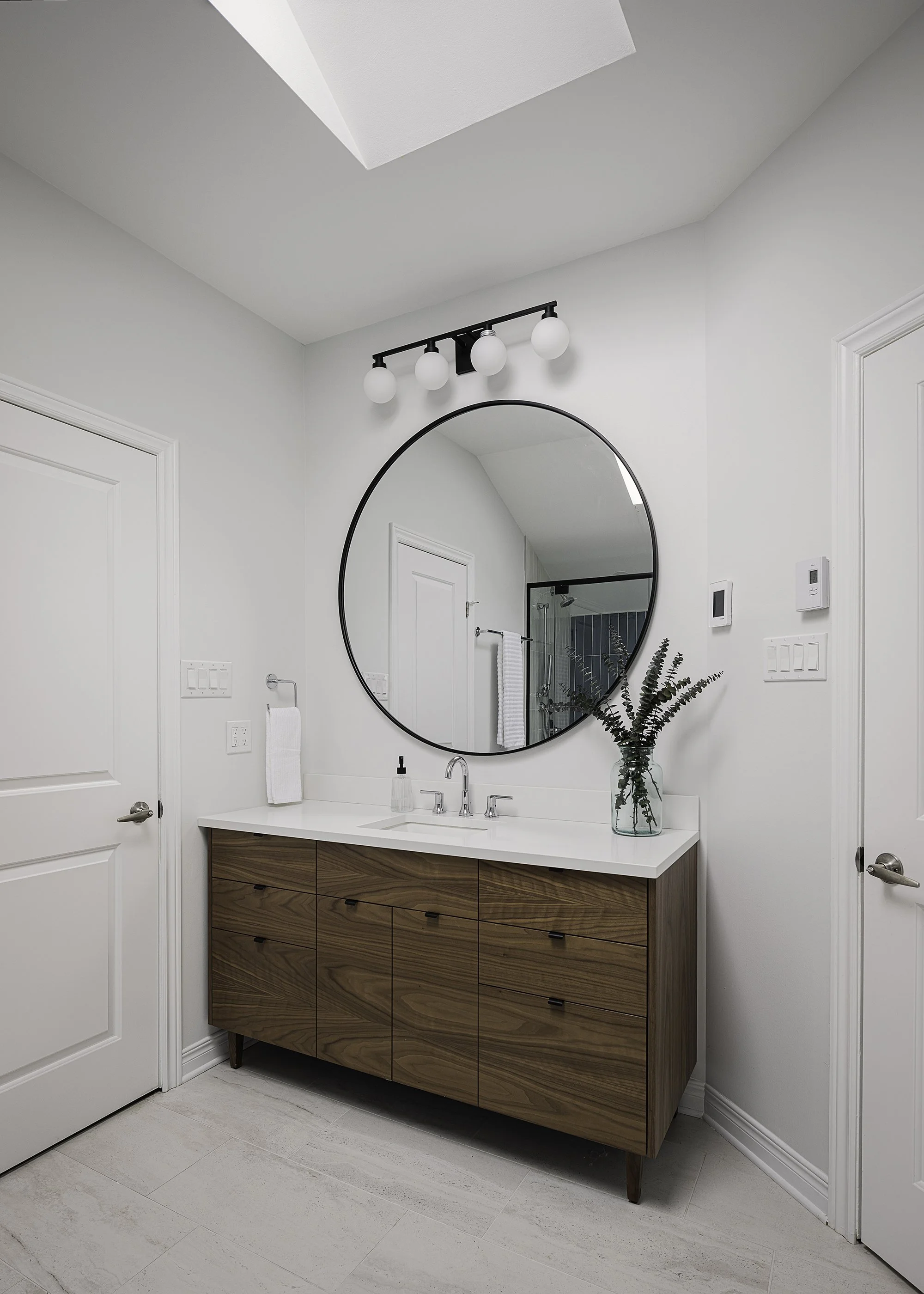 Ensuite bathroom renovation in Ottawa featuring a walnut vanity and oversized round mirror. 