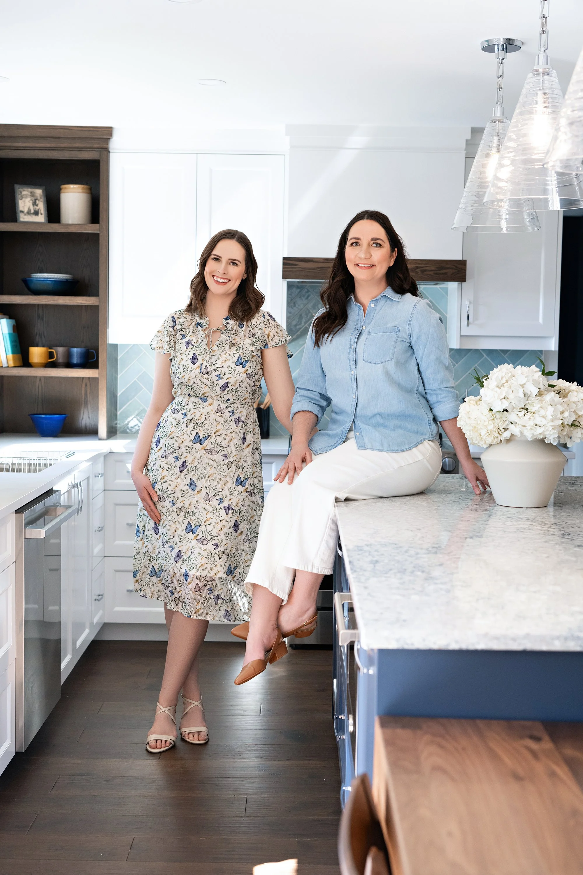 Megan Patterson and Natalie Cox, co-owners of CPI Interiors, an Ottawa interior design firm are standing in a white custom kitchen with medium oak floors.