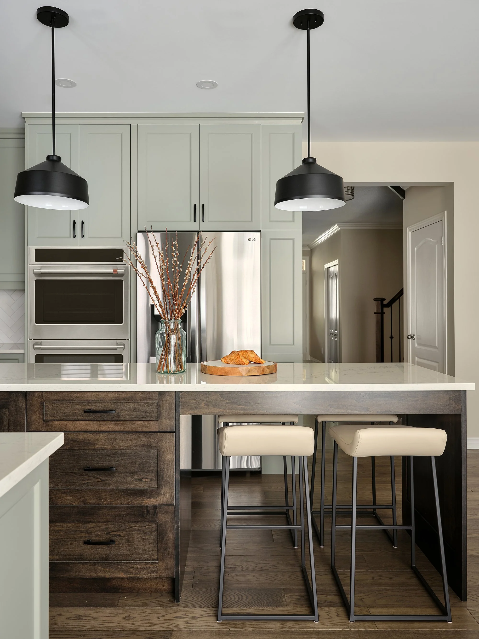 Custom kitchen renovation in Ottawa featuring warm green shaker cabinetry and black pendants over the island. 