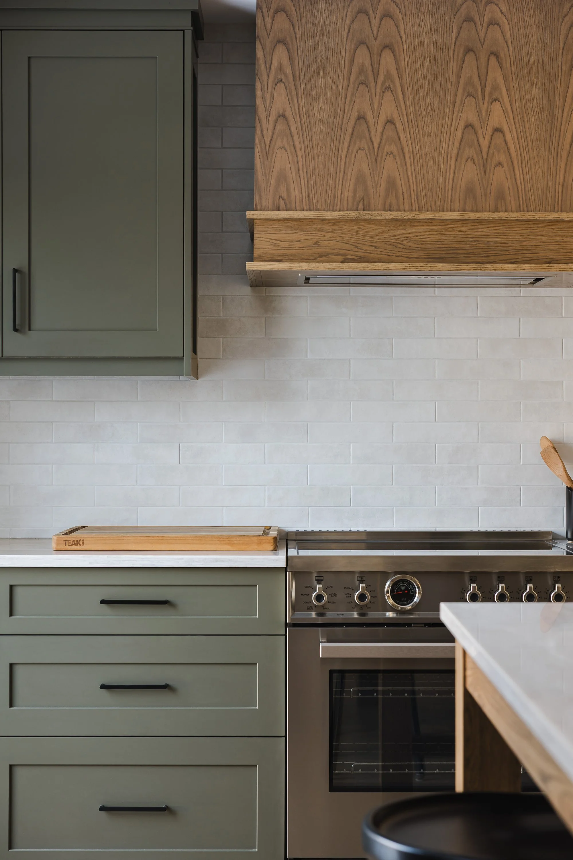 Custom kitchen renovation in Ottawa featuring green shaker cabinets, black hardware and a white oak custom decorative hood fan. 