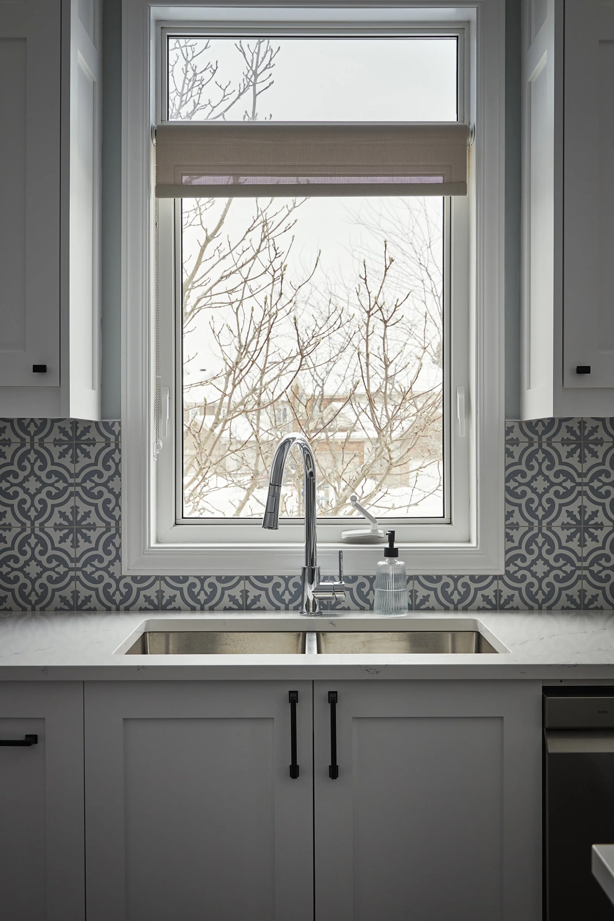 Custom kitchen renovation in Ottawa featuring white shaker cabinets and a sink in front of a window. 