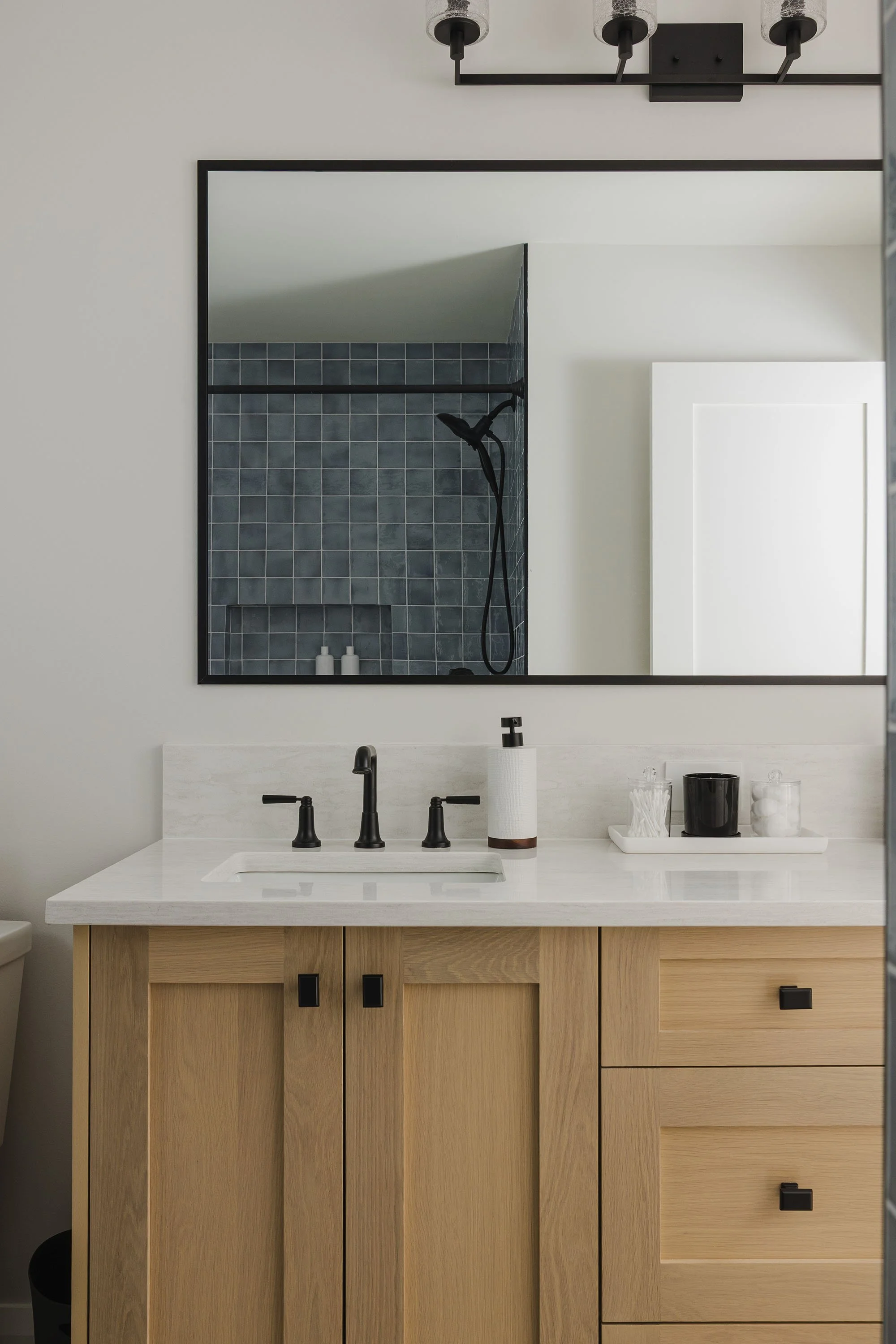 Bathroom renovation in Ottawa featuring a white oak vanity and blue shower tile with black accents. 