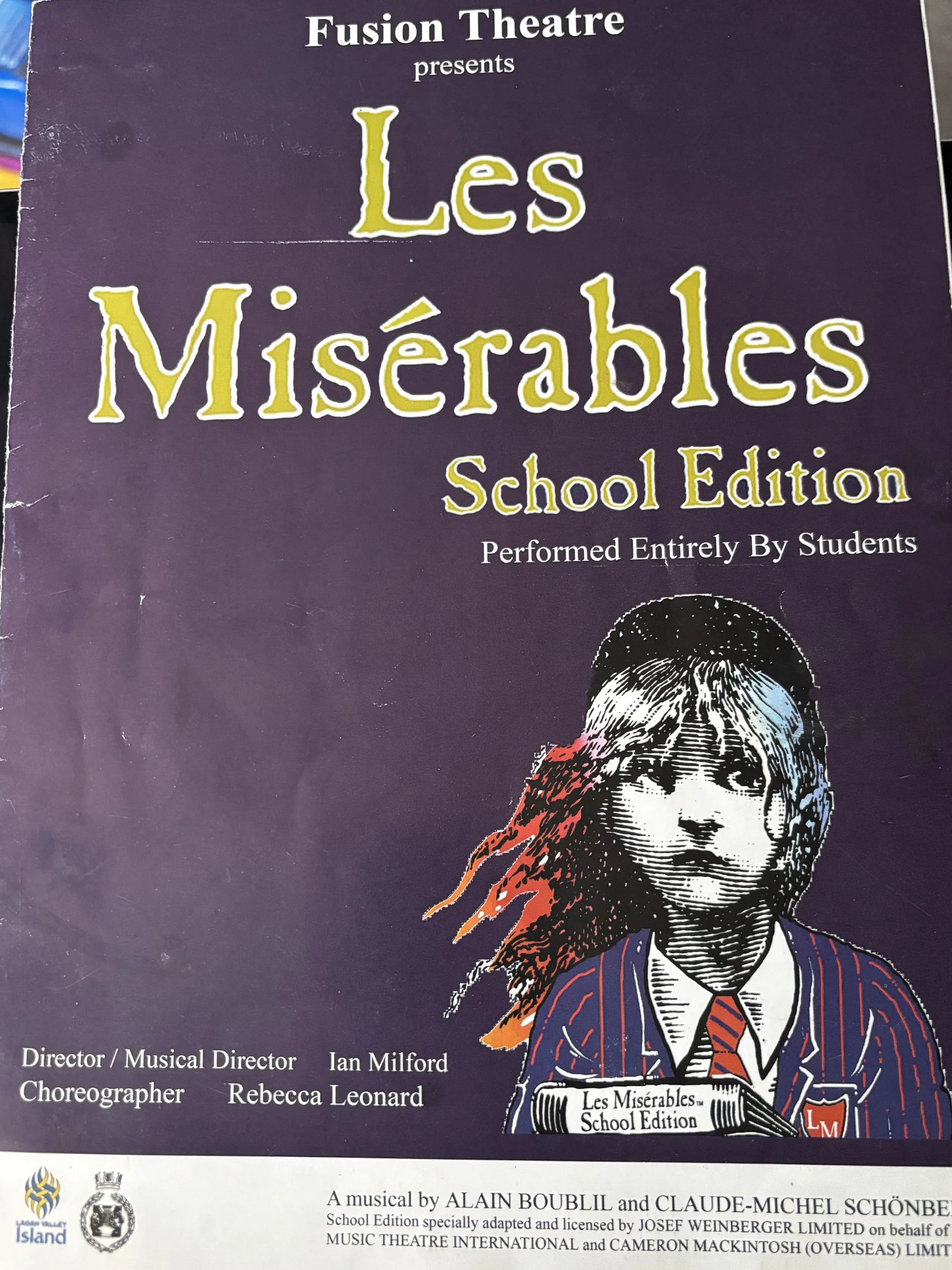 Illustration of a young girl with watercolors in the background, red on the right and blue on the left, with the title 'Les Miserables' in gold lettering and a gold emblem in the top right corner.