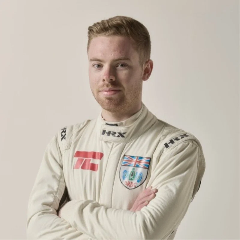 A young man with short blonde hair and a black athletic shirt smiling and looking to the side in what appears to be an indoor sports or fitness facility at night.