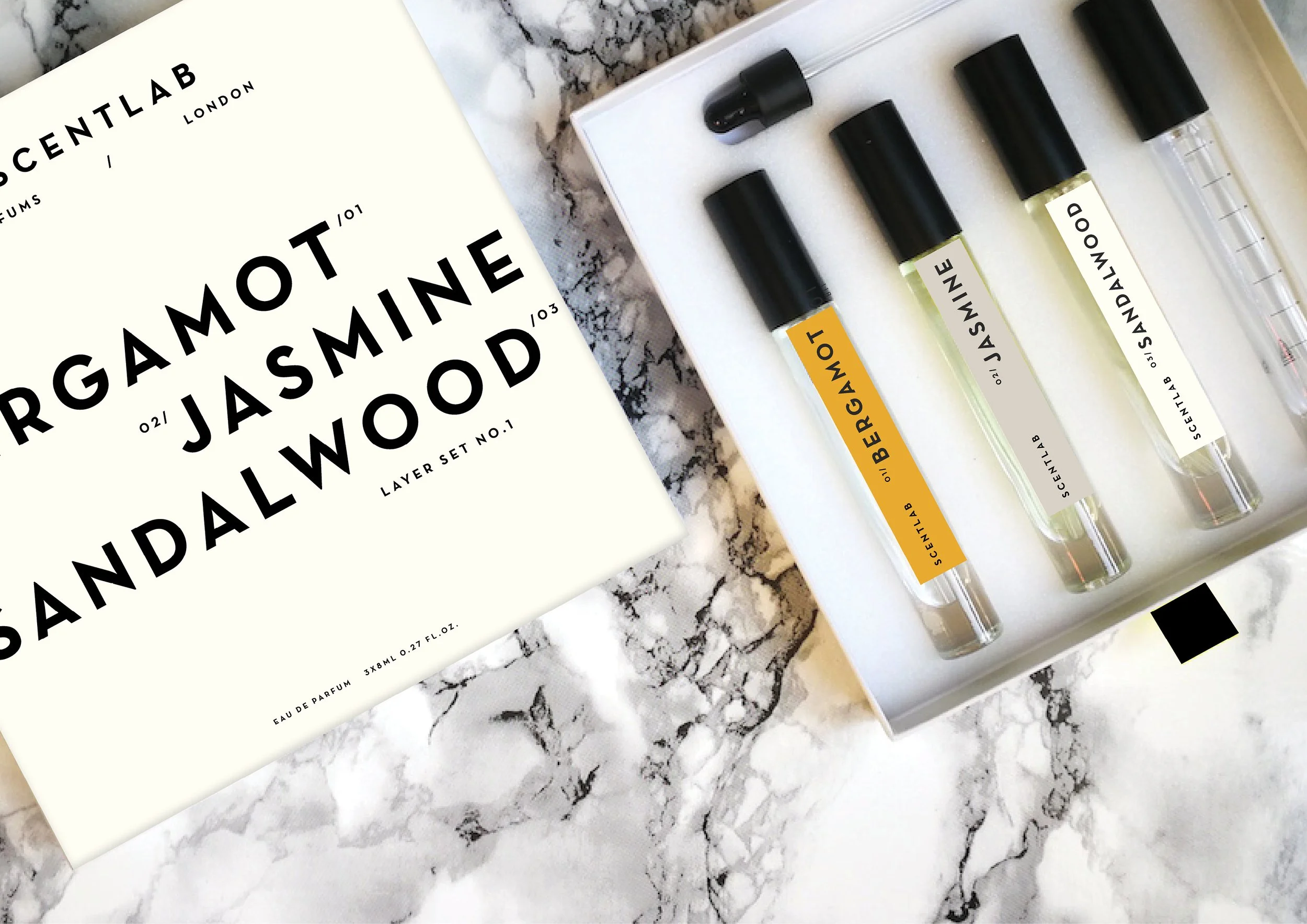 A set of four perfume samples in glass vials with black caps and a cardboard box labeled 'Scenglabs' on a marble surface.