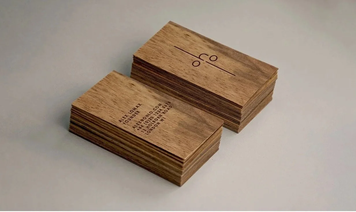 Two stacks of wooden business cards with engraved text and logos on a light surface.