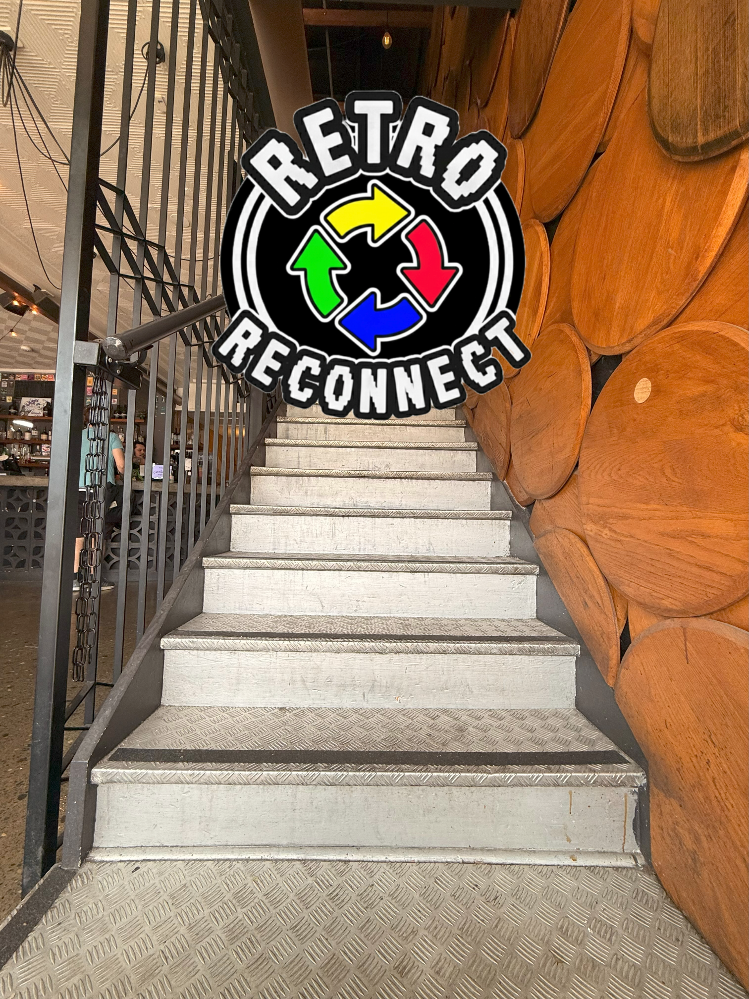 Metal staircase leading to an upper level, with a wooden log wall on the right and a black gated railing on the left, with a 'Retro Reconnect' sticker overlayed.