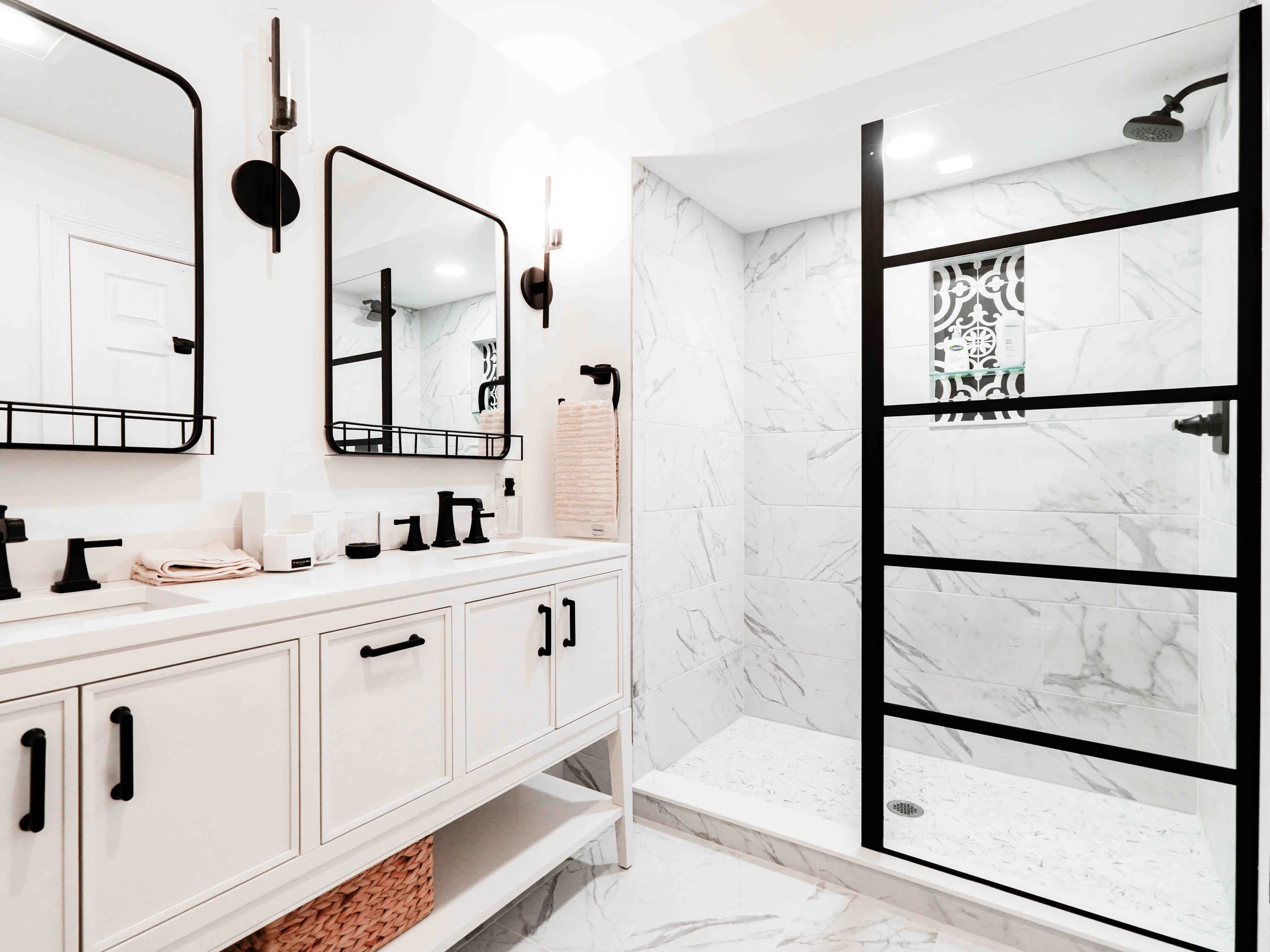 modern bathroom with white cabinetry, black hardware, and a marble shower with a black metal-framed glass door.