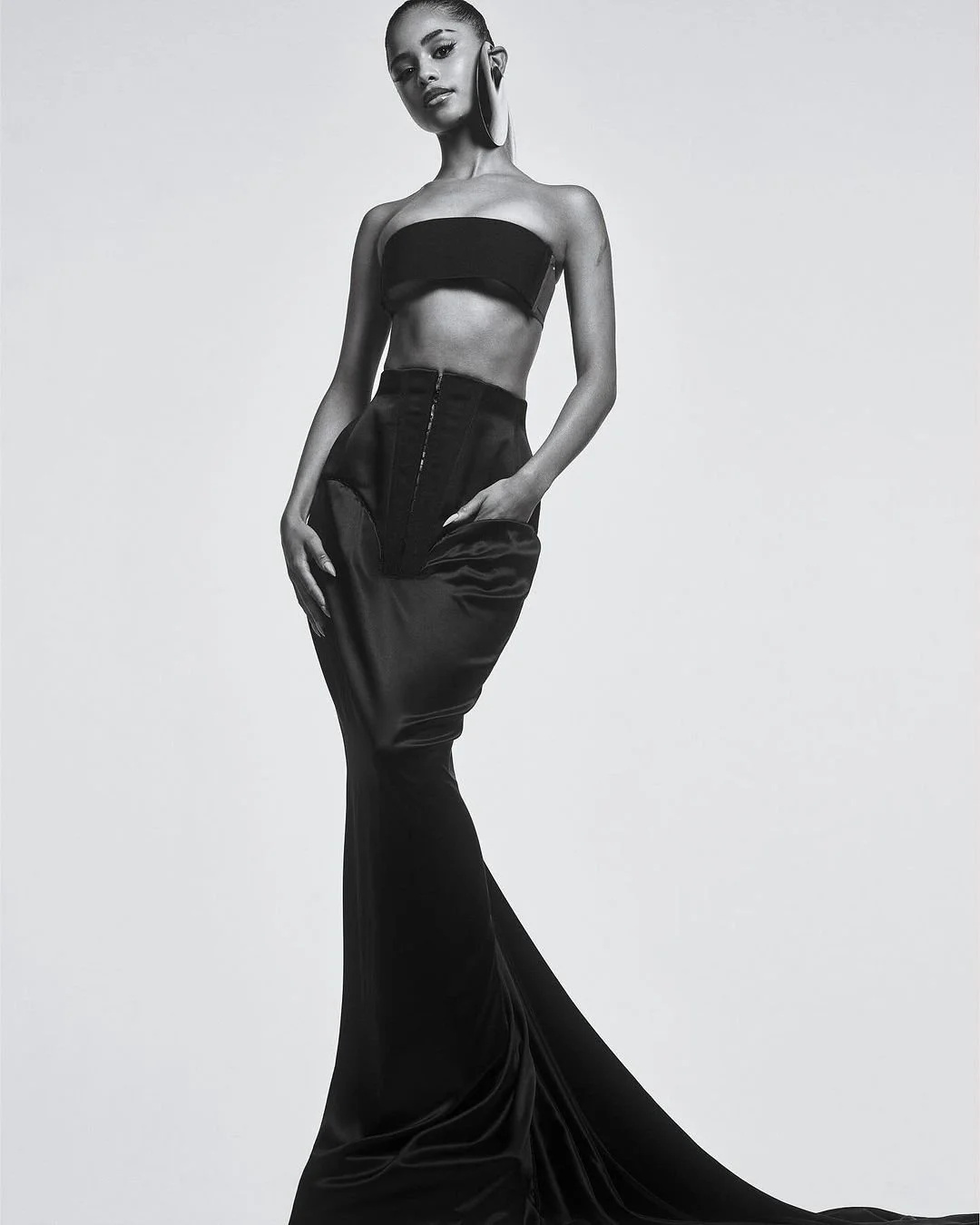 Une femme portant un haut court sans manches et une jupe longue en satin noir, debout contre un fond blanc.