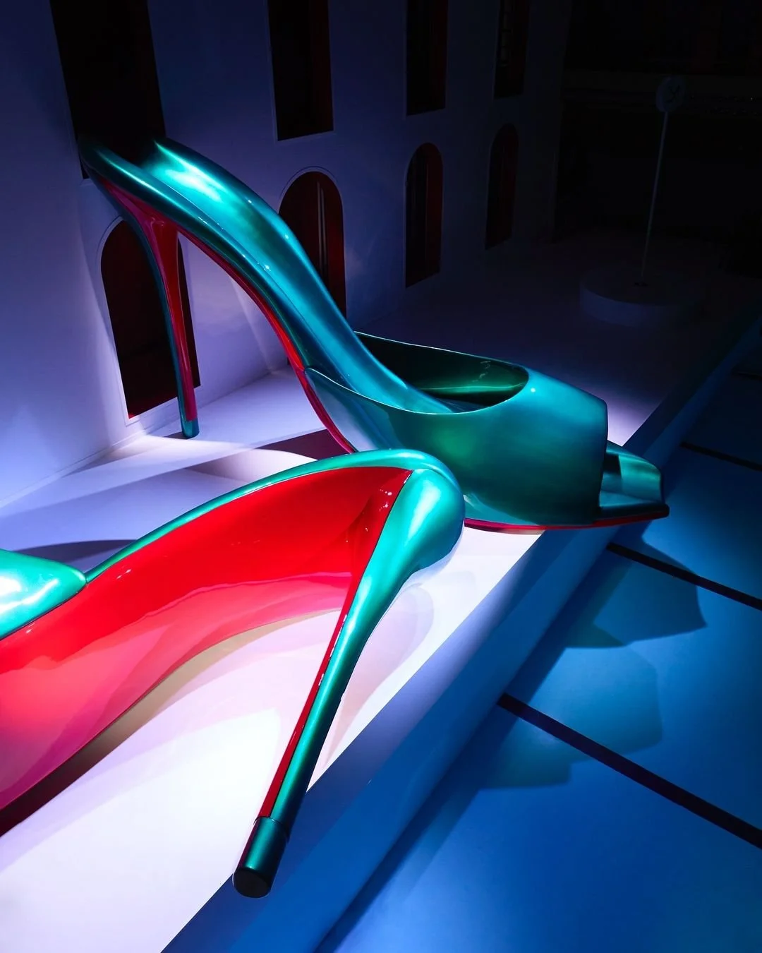 Une paire de talons hauts en verre coloré, affichés dans une vitrine avec un éclairage dramatique.