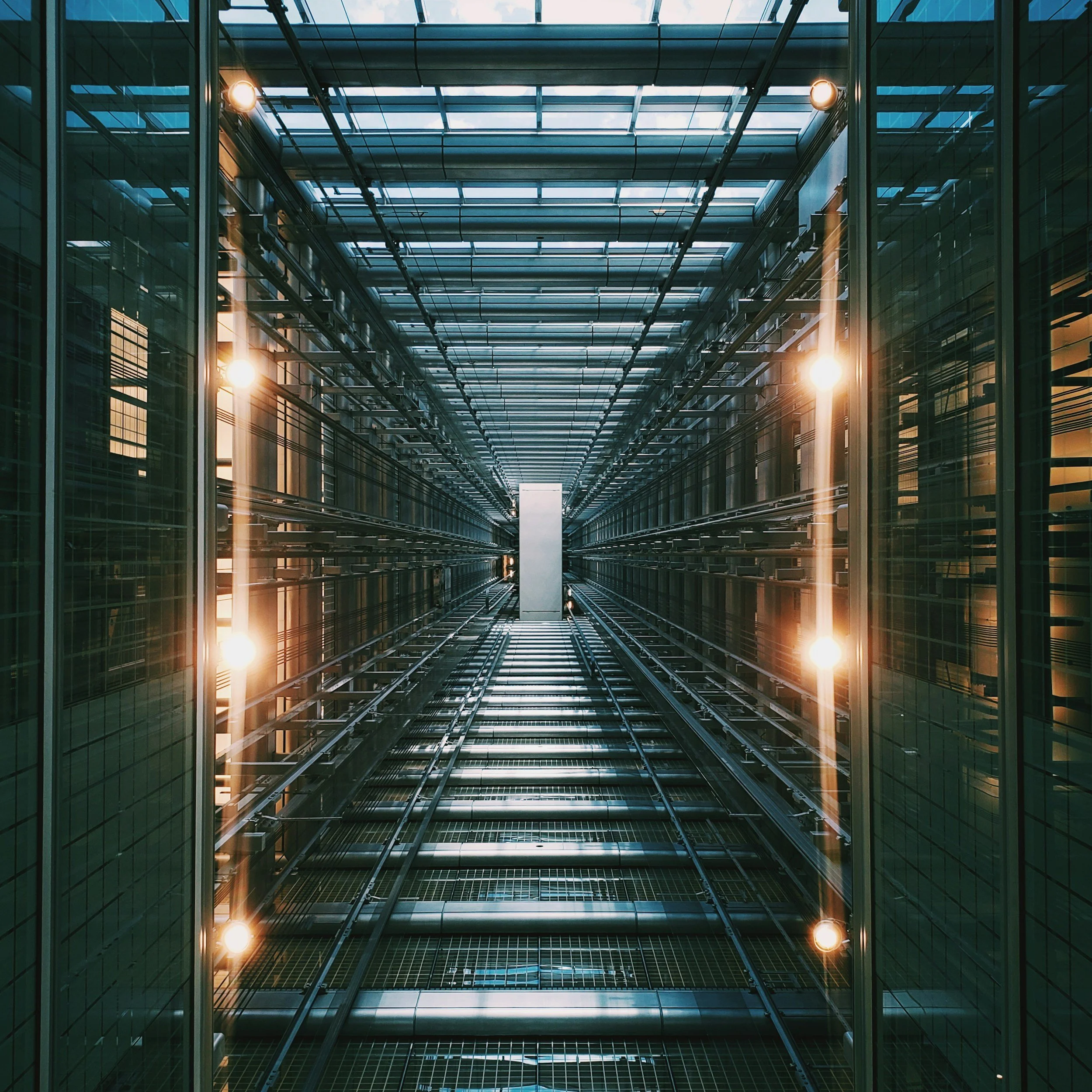 Looking up inside a modern glass elevator with metallic railings and lighting.
