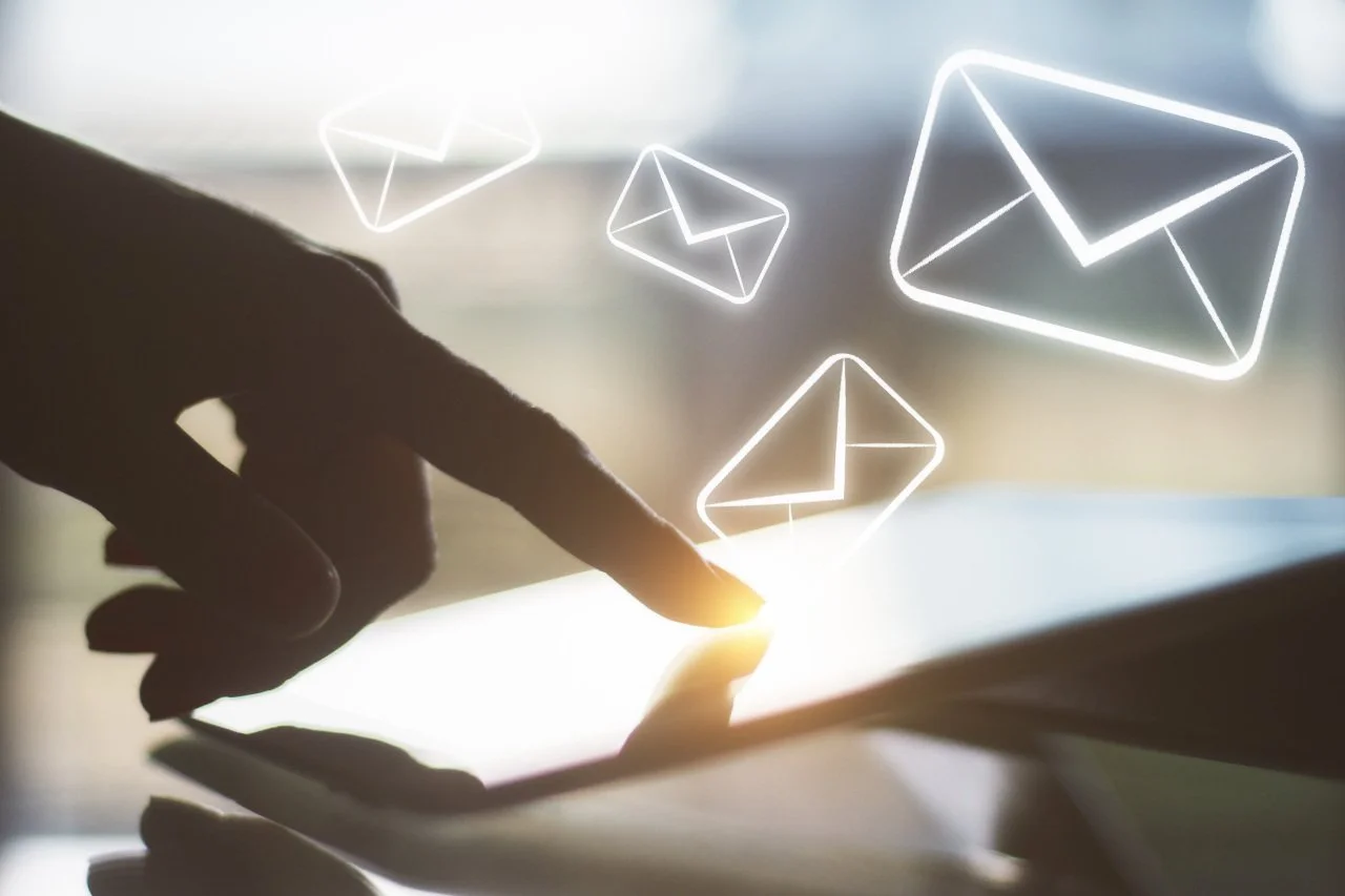 Illustration of a person using a touchscreen device with floating digital email icons above, representing email communication.