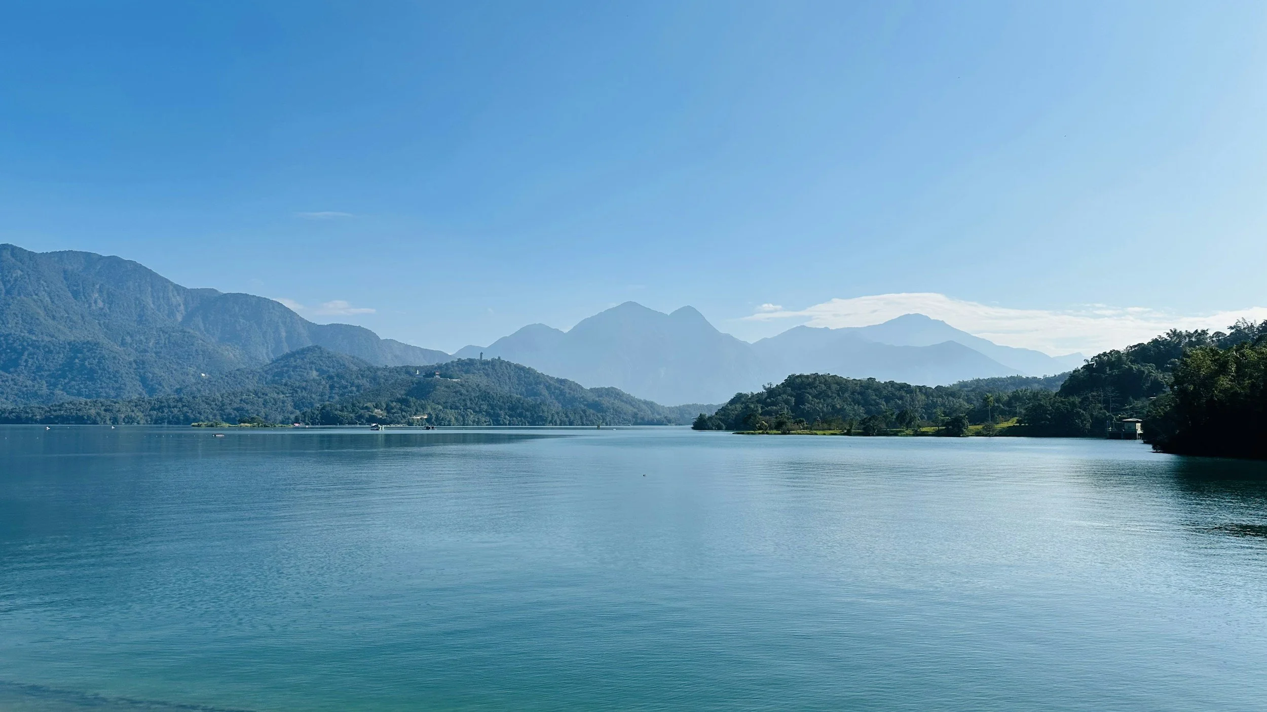 Un lac entouré de montagnes verdoyantes sous un ciel clair et ensoleillé.