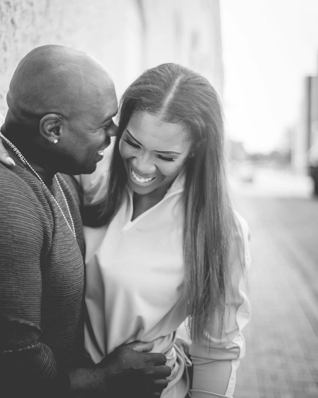 Two people, a man and a woman, laughing and leaning into each other outdoors.