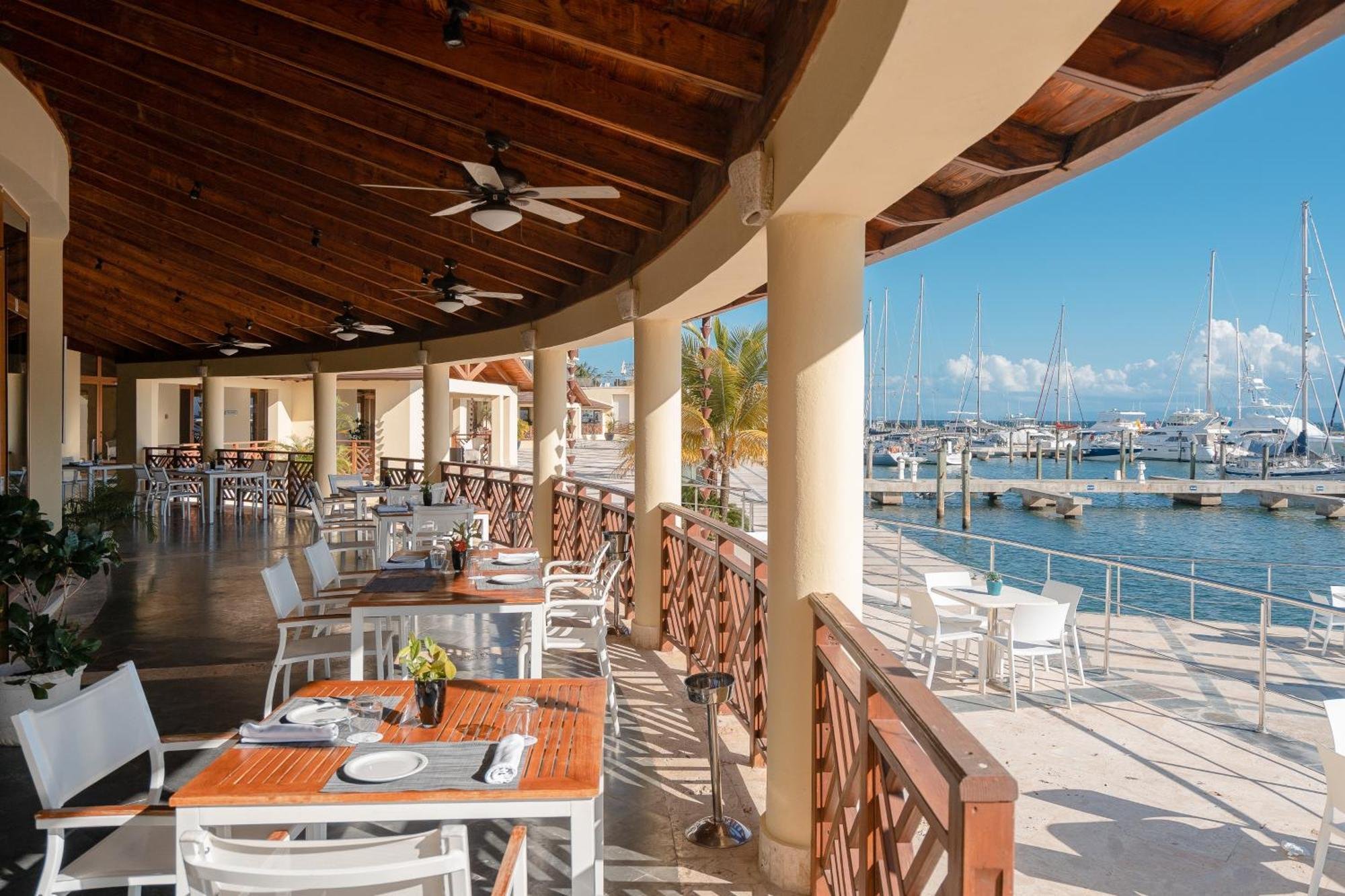 Open-air restaurant overlooking marina with boats, white tables and chairs, and a wooden ceiling.