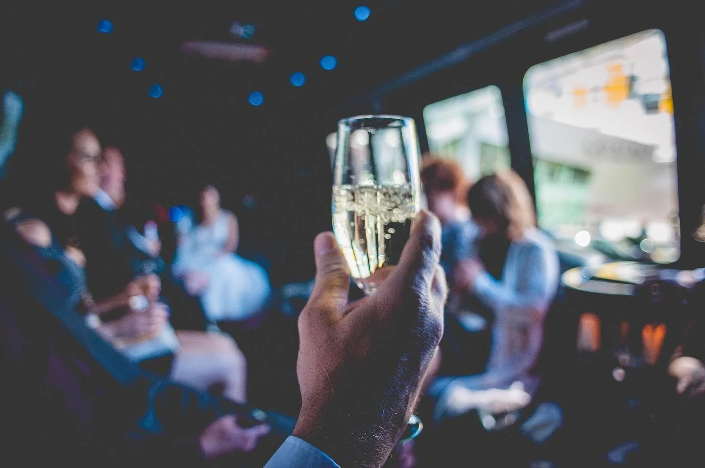 A person holding a glass of champagne in a dimly lit bus with people in the background.