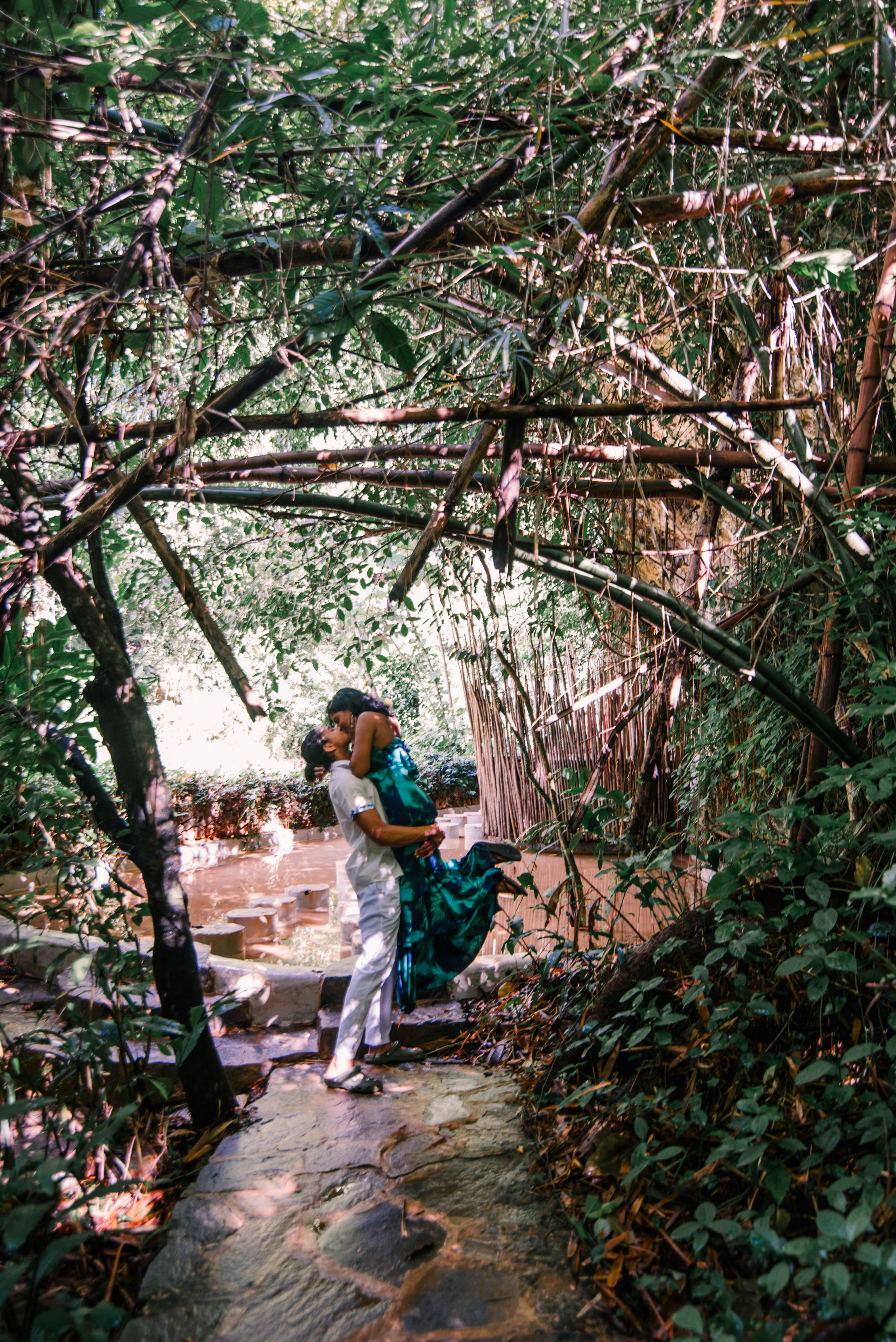 A couple in wedding attire sharing a kiss in a lush, green jungle setting.