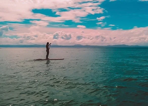 Person paddleboarding on a calm ocean under a partly cloudy sky.